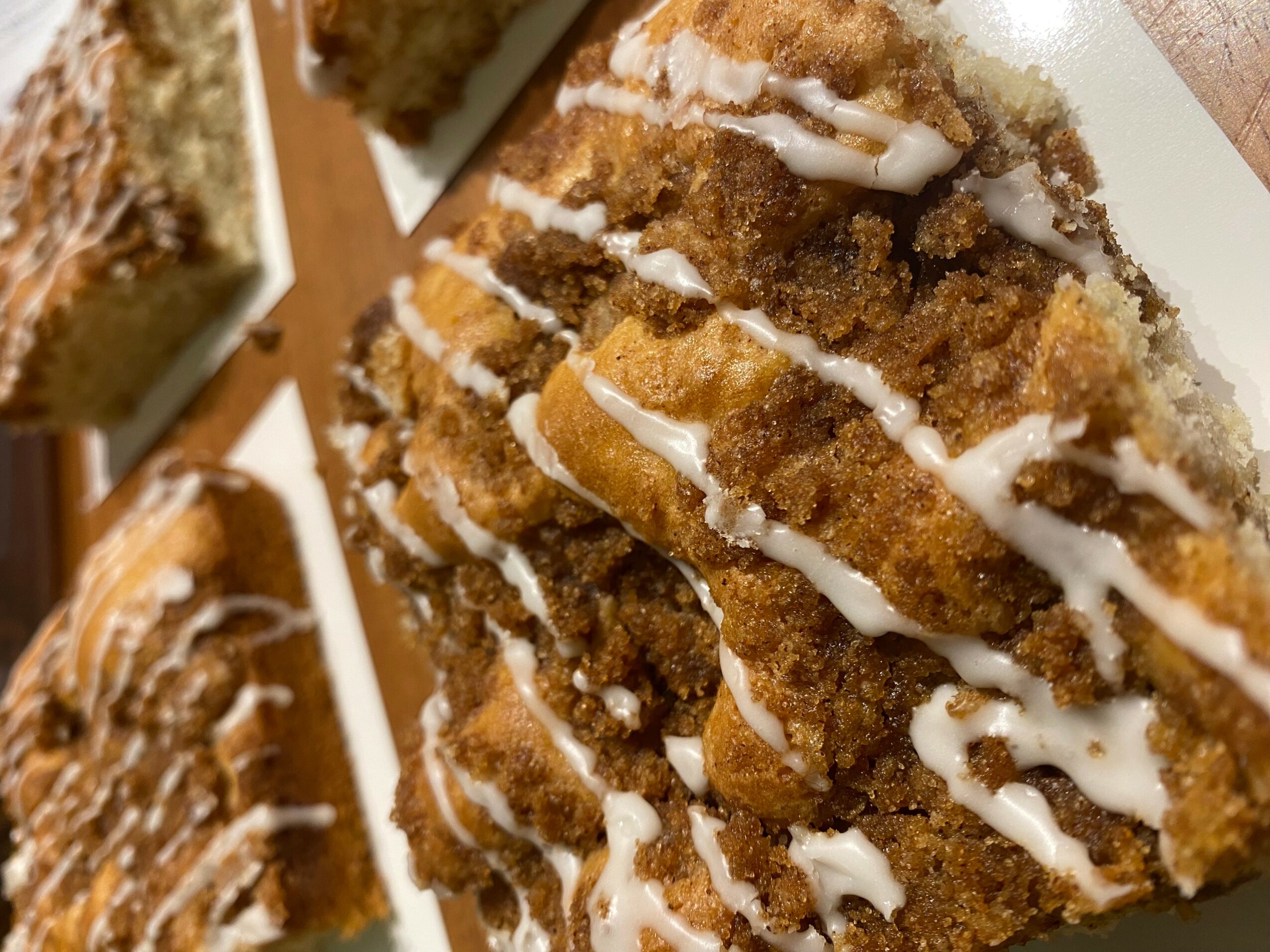 Close-up of breaded fried food with white drizzle on top, on a white plate, with other similar items in the background.