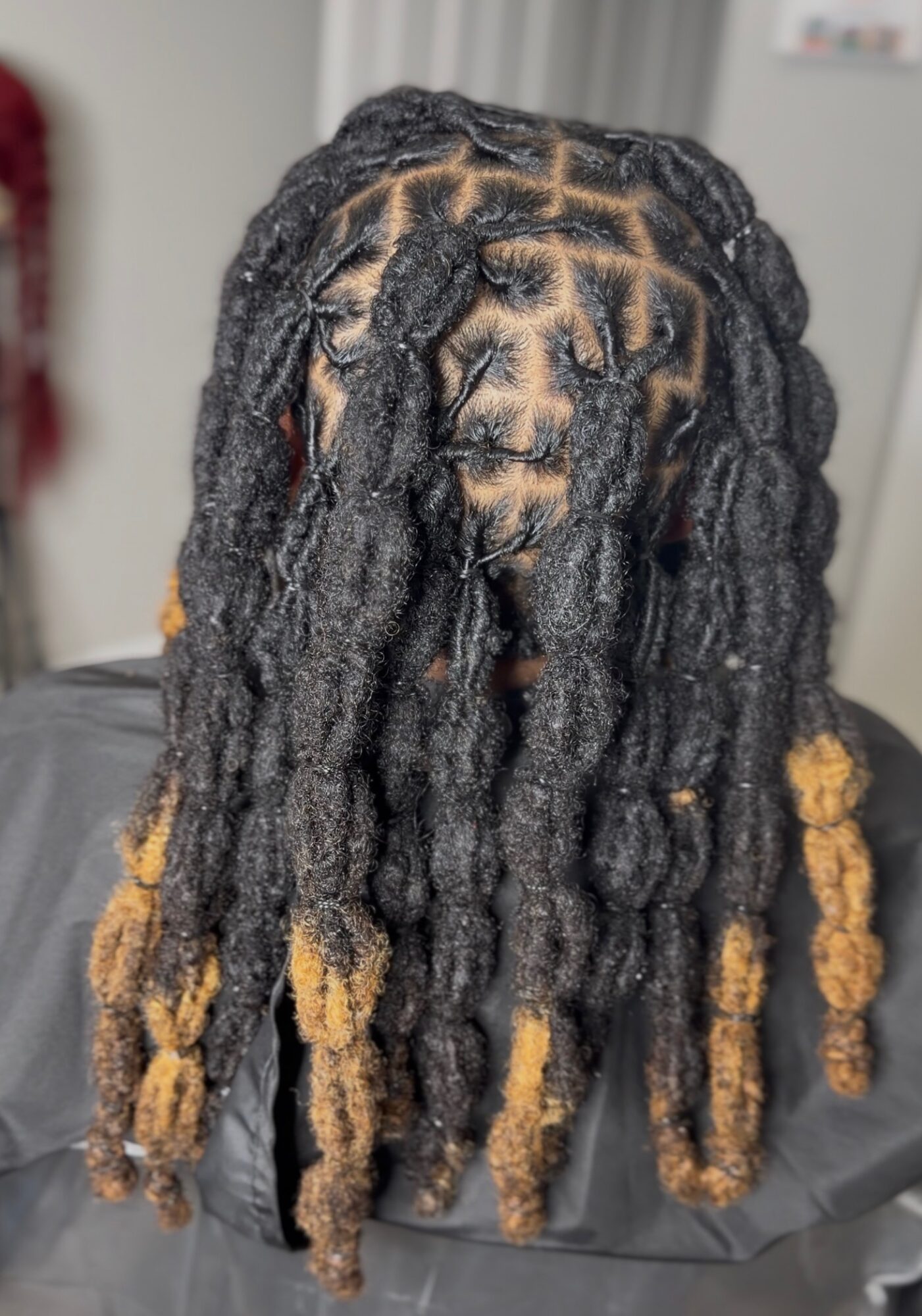 Person with long dreadlocks, some dyed blonde, covering face, indoors, background blurred.