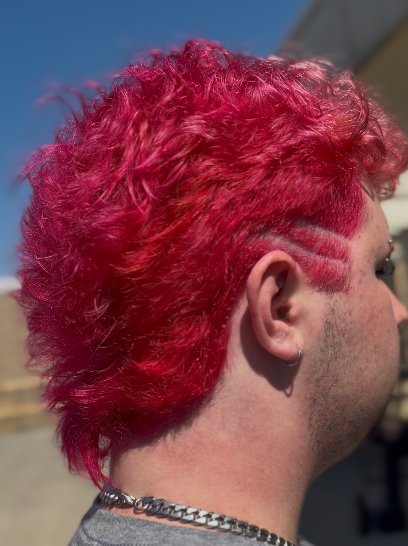 Side view of a person with bright pink, curly hair and a shaved design on the side of the head.