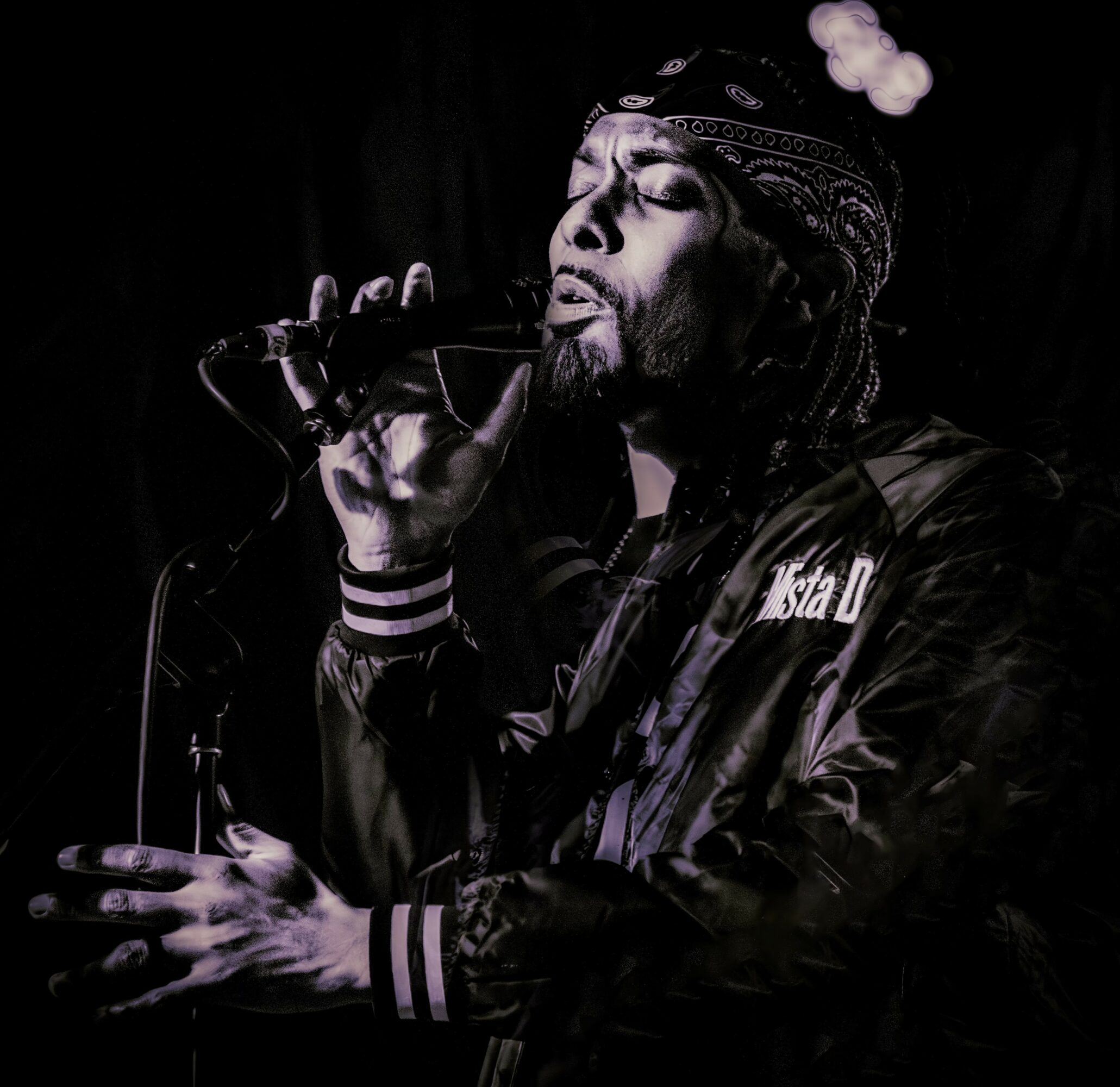 Person singing into a microphone, wearing a headband and jacket, with a dark background.