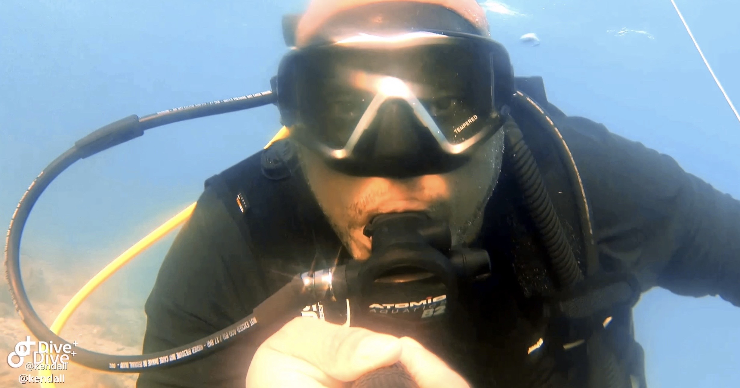 Close-up of a scuba diver underwater wearing a mask and breathing apparatus, with a yellow hose visible.