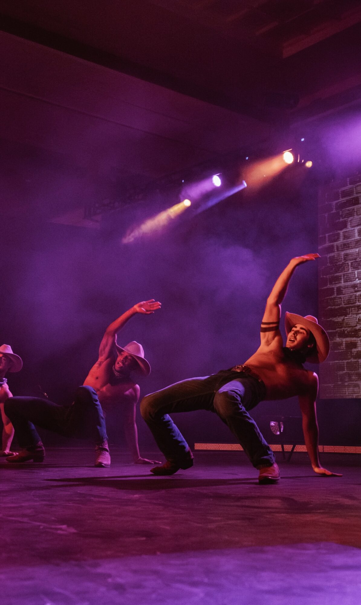 Group of dancers performing on stage with colorful lighting and smoke effects, one dancer in a backbend pose.