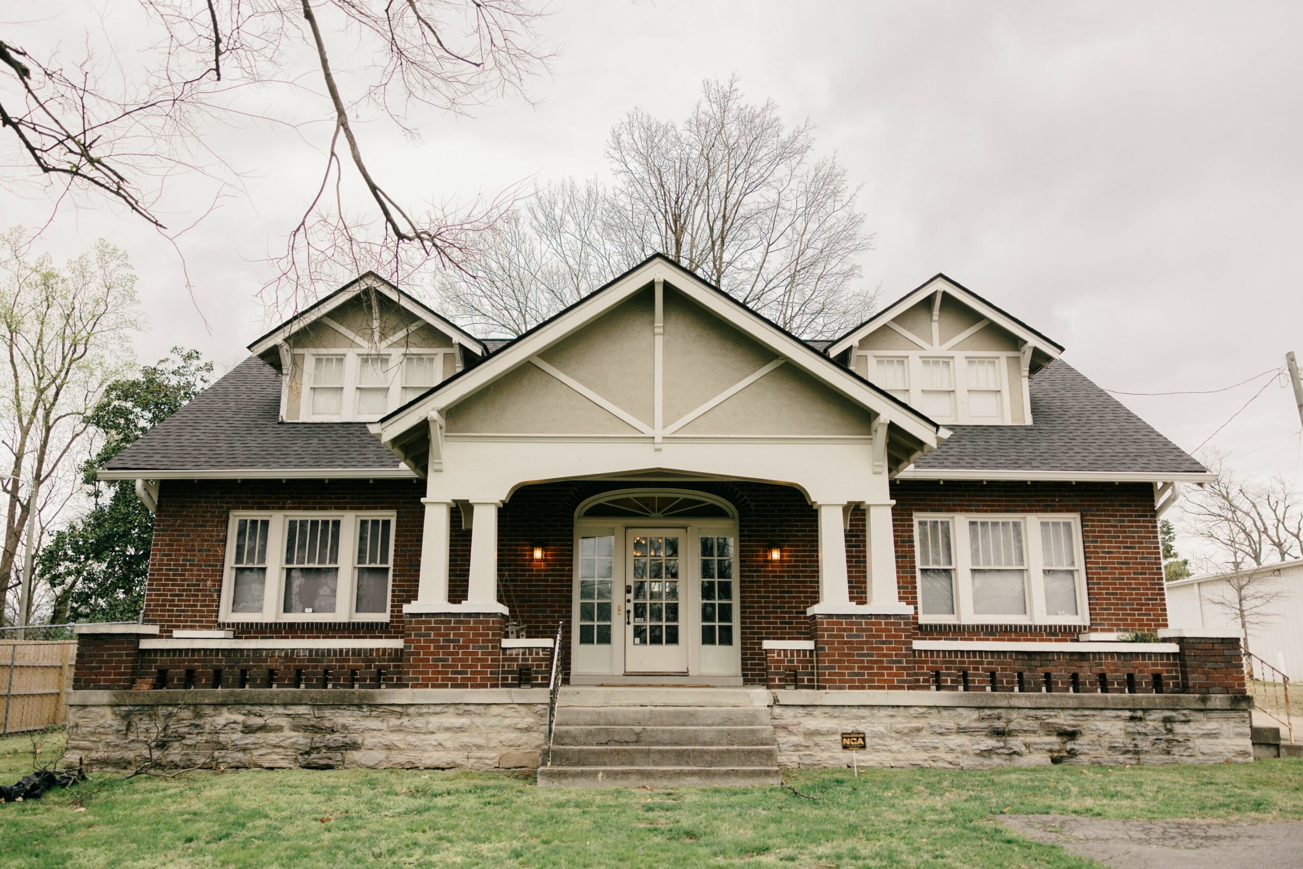 Large house with front porch, brick and white siding, multiple windows, and a staircase leading to the entrance.