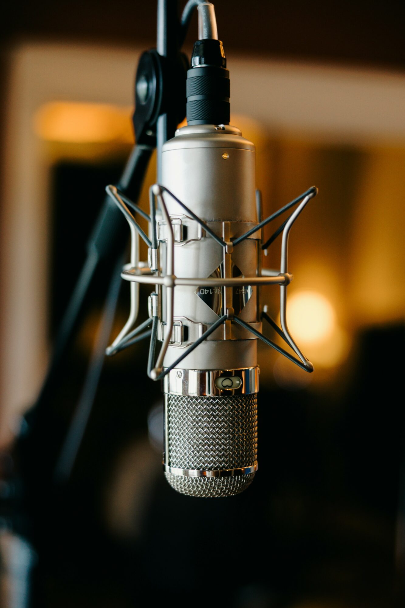 Studio microphone with shock mount and pop filter in recording environment, blurred background with warm lighting