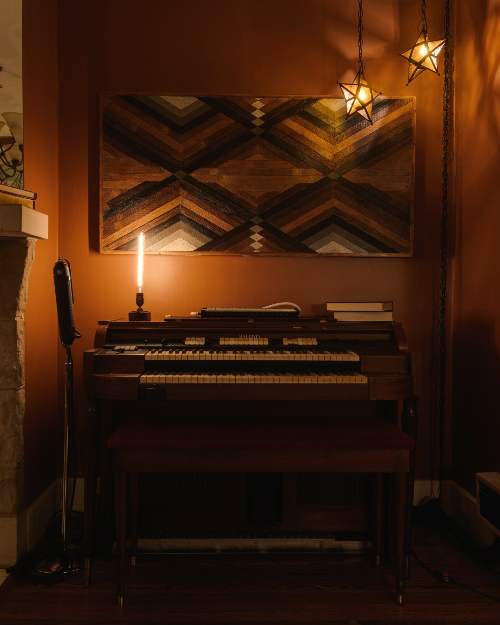 Upright piano with a bench in a warmly lit room, decorated with star-shaped hanging lights and a geometric wall art.