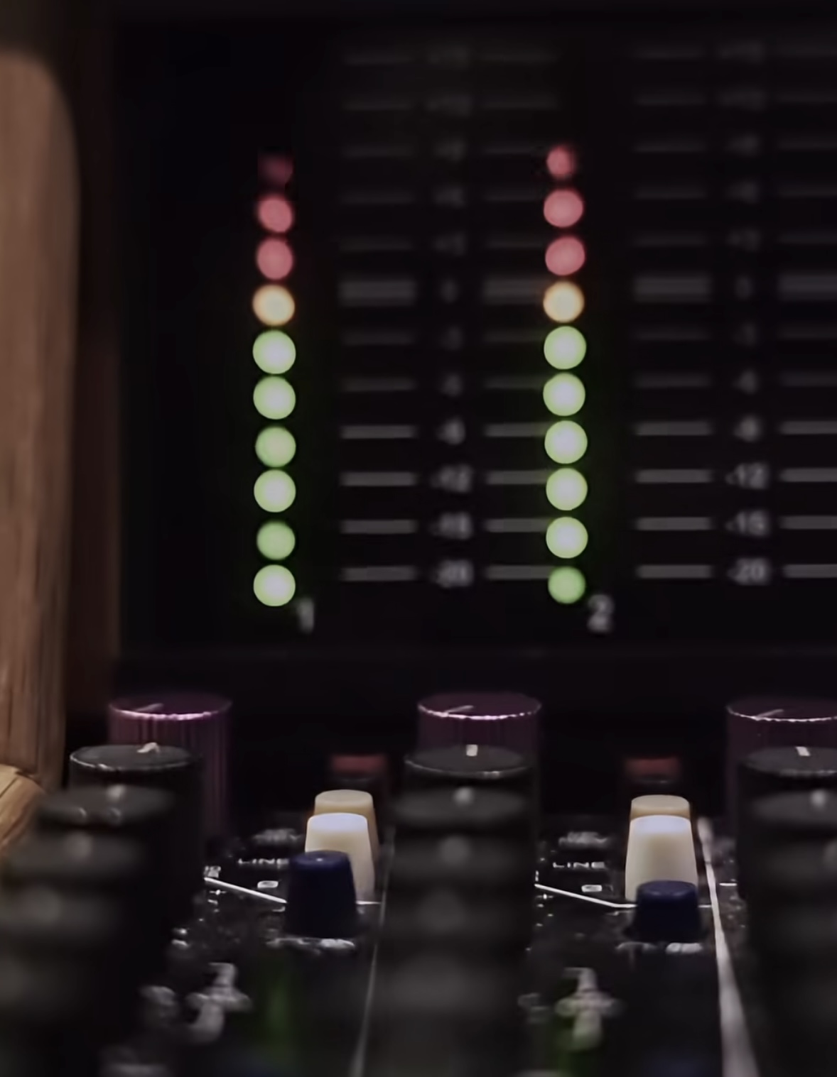 Audio mixing console with sliders and a dark background, illuminated by colorful lights, viewed from above.