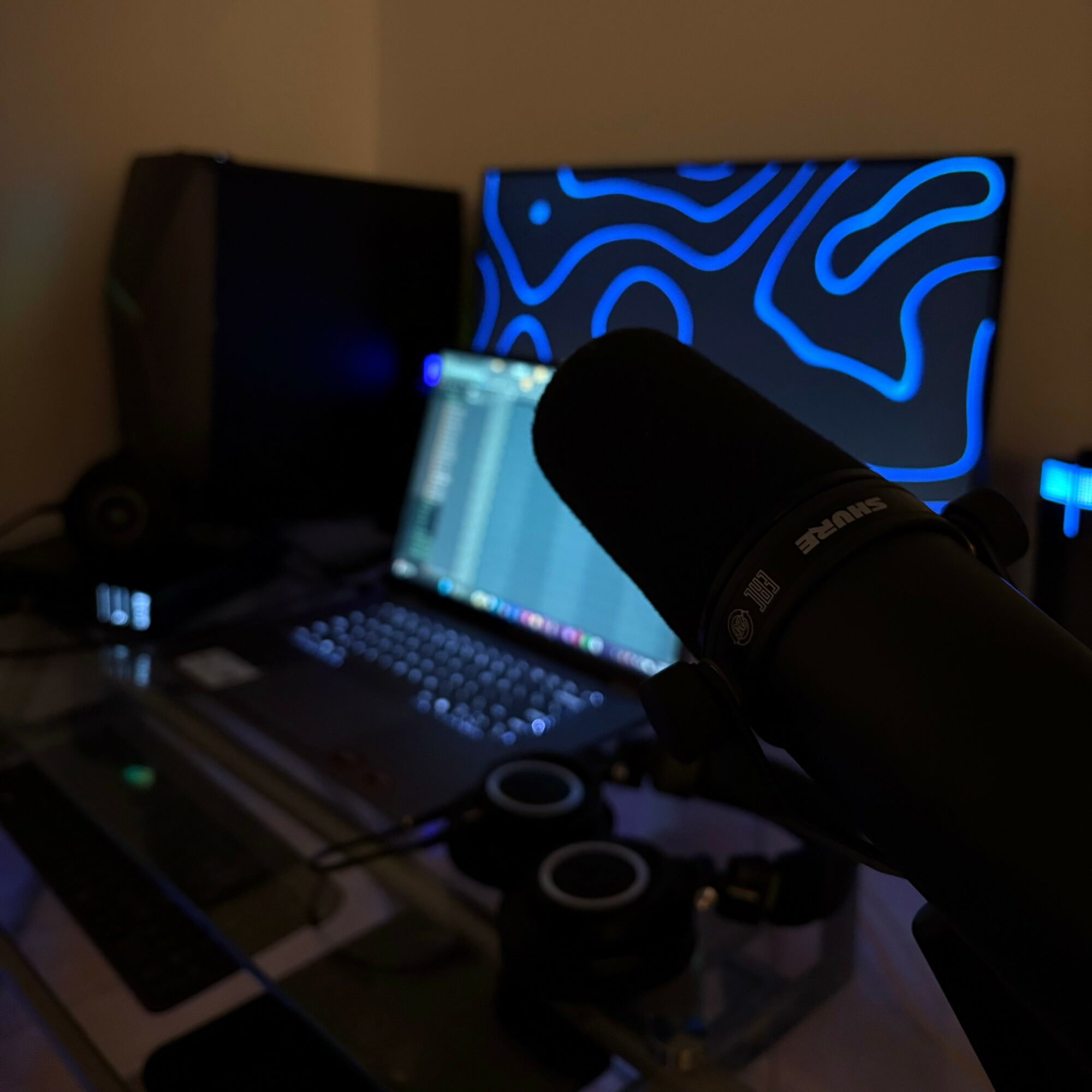 Microphone directed at a laptop with a blue abstract screen in a dimly lit room.