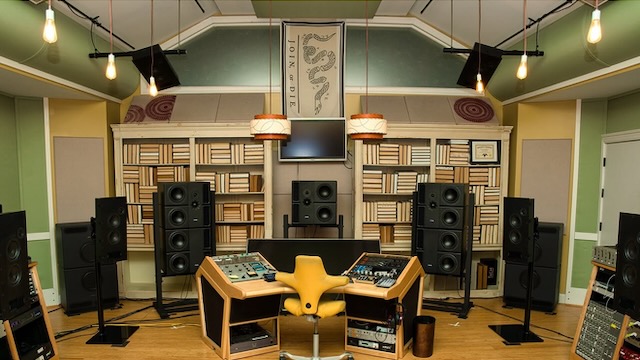 Recording studio with speakers, soundproofing, and a central desk with a yellow chair, in a colorful room.