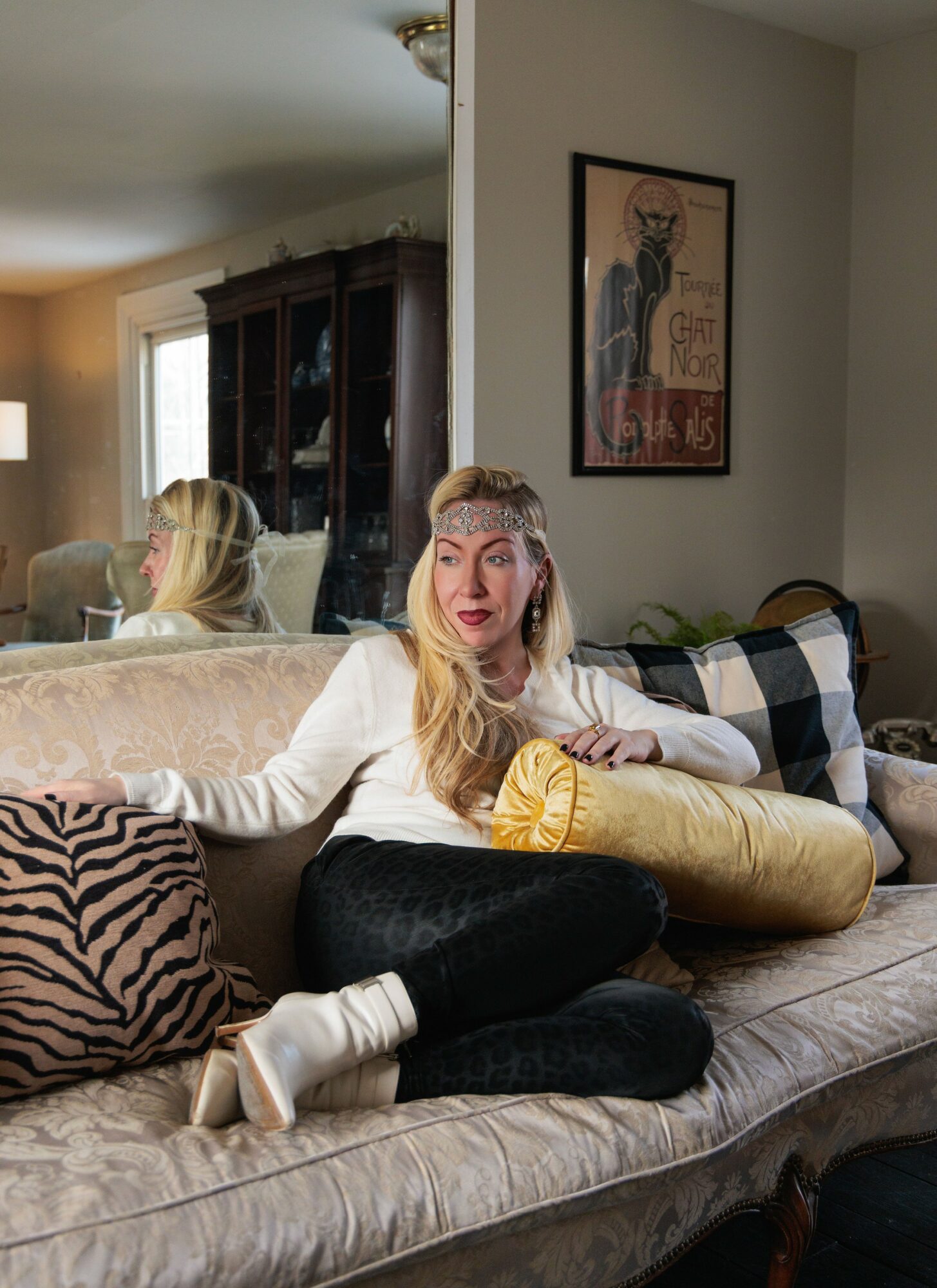 Woman with long blonde hair sitting on a sofa, holding a yellow pillow, with a zebra print pillow nearby, in a living room.