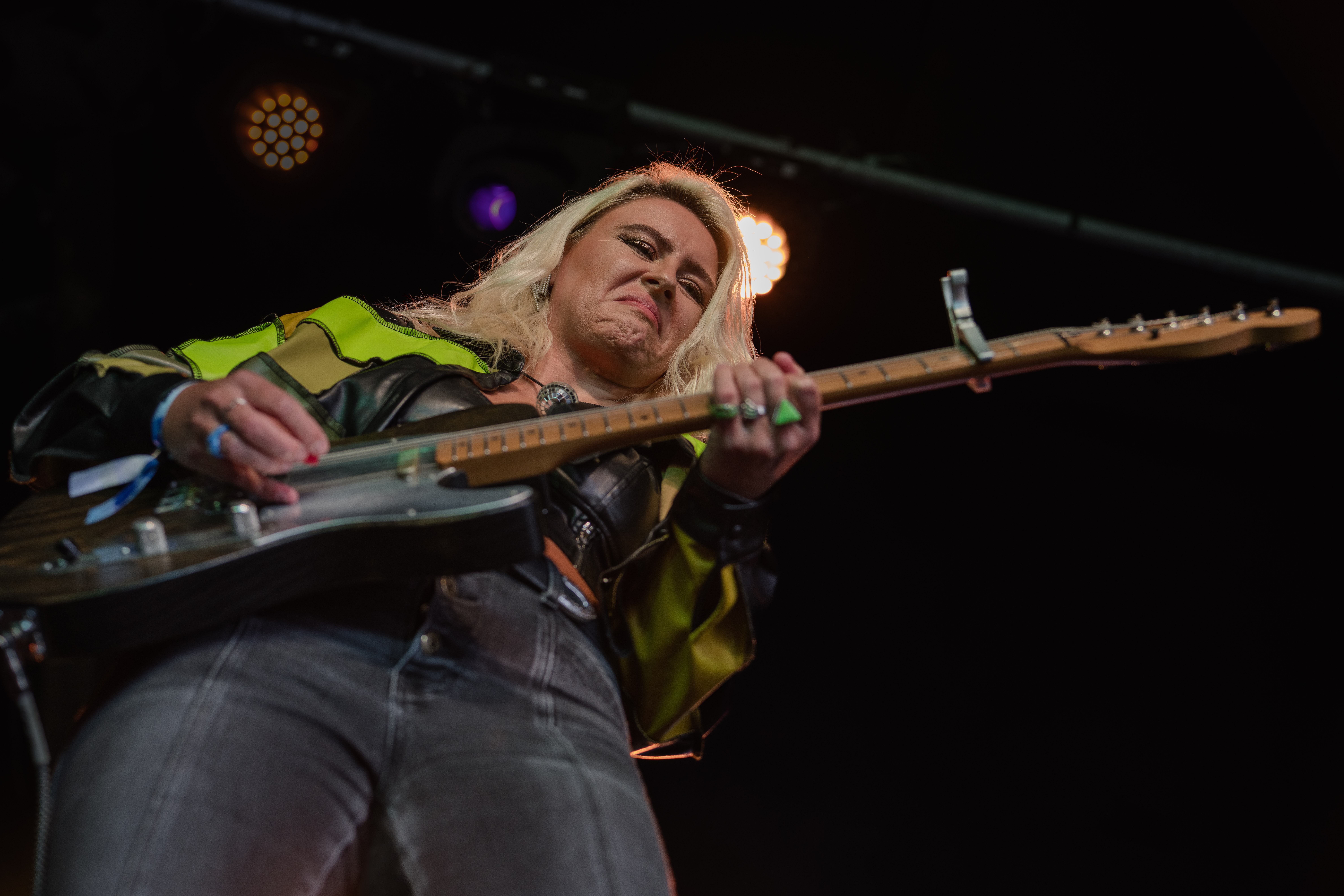 Woman playing electric guitar on stage with stage lights in background.