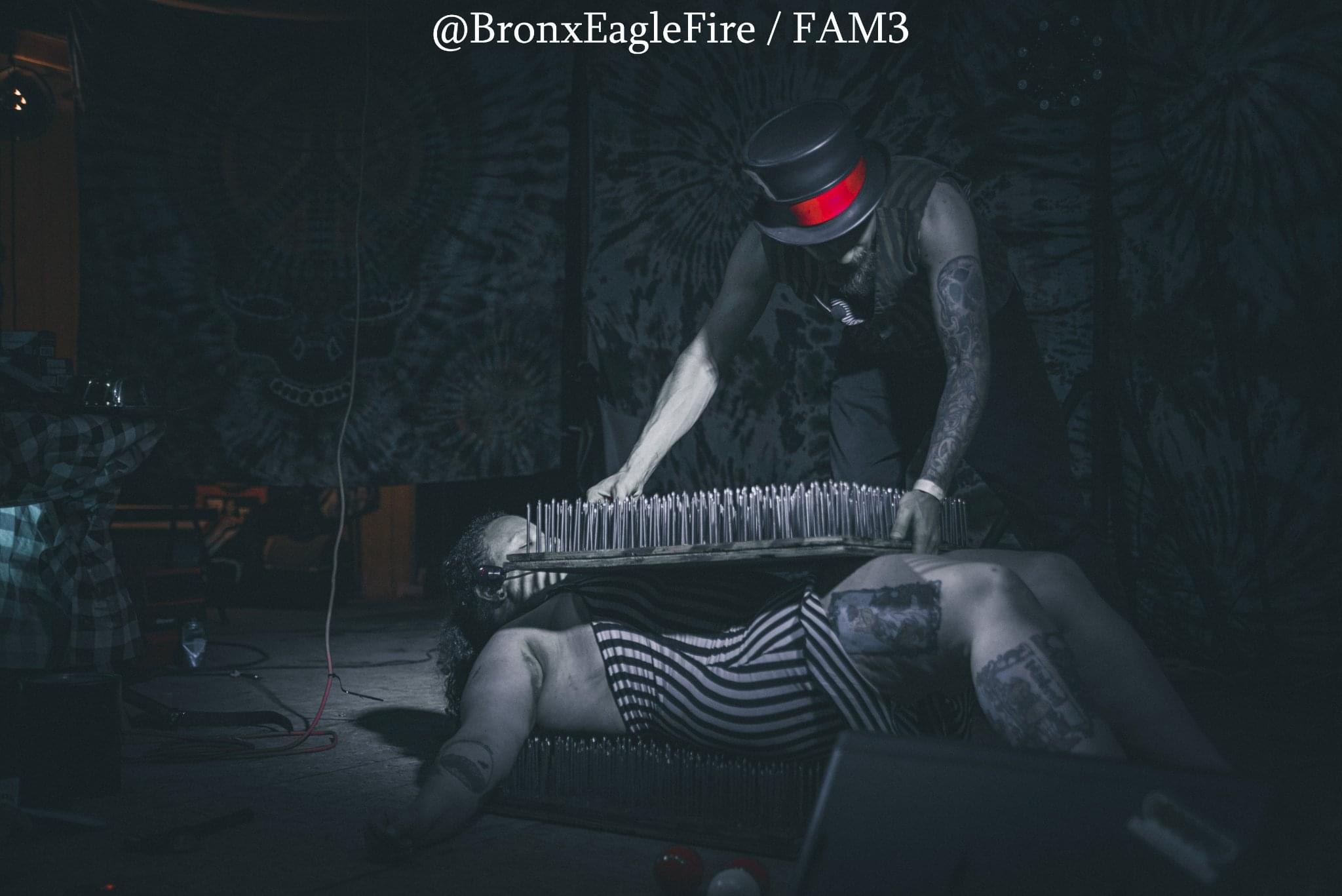 Person lying on the floor with a striped outfit, another person standing with a keyboard, dark background, dim lighting.