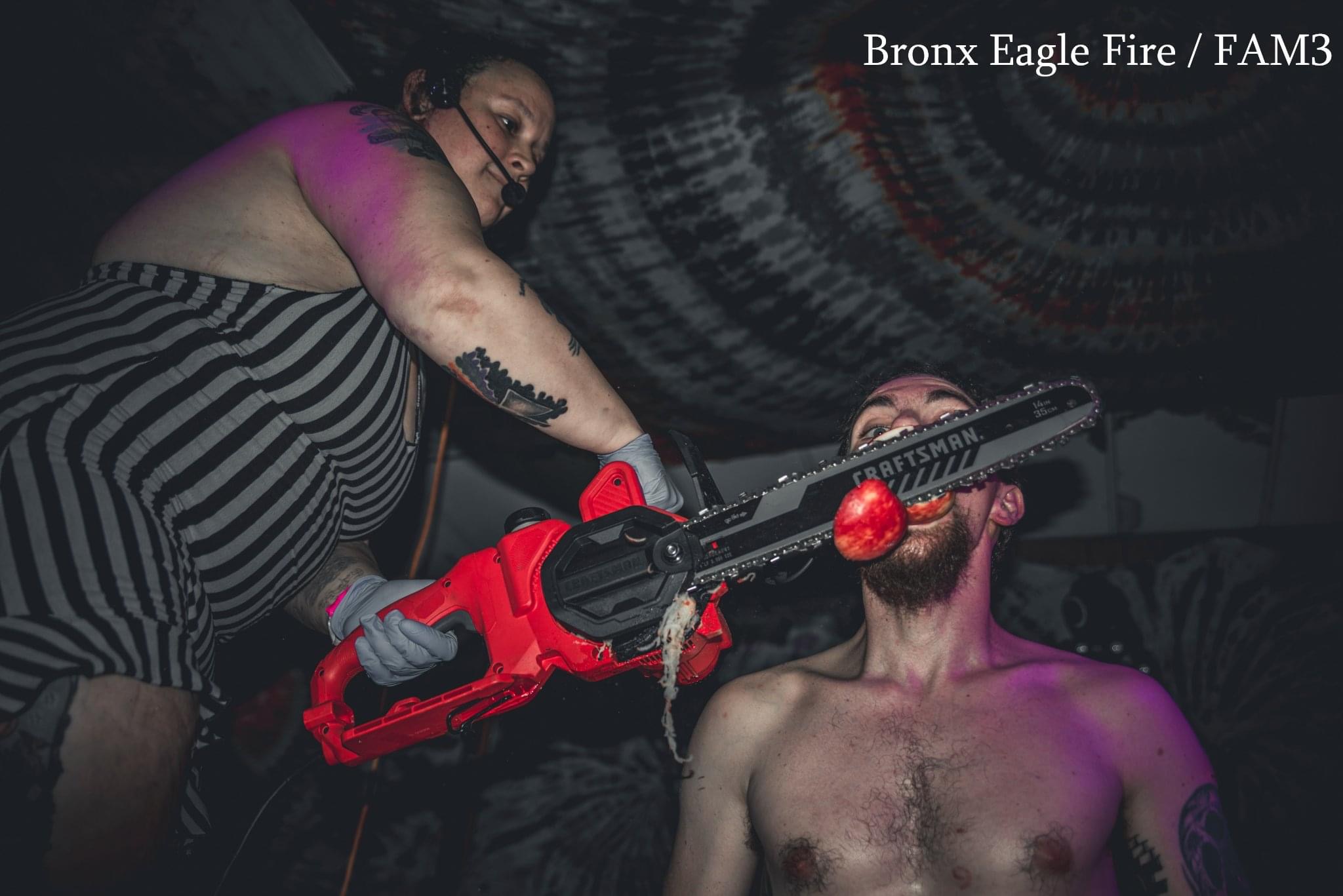 Person holding a red and black toy gun aimed at another person with a bare chest, in a dark setting.