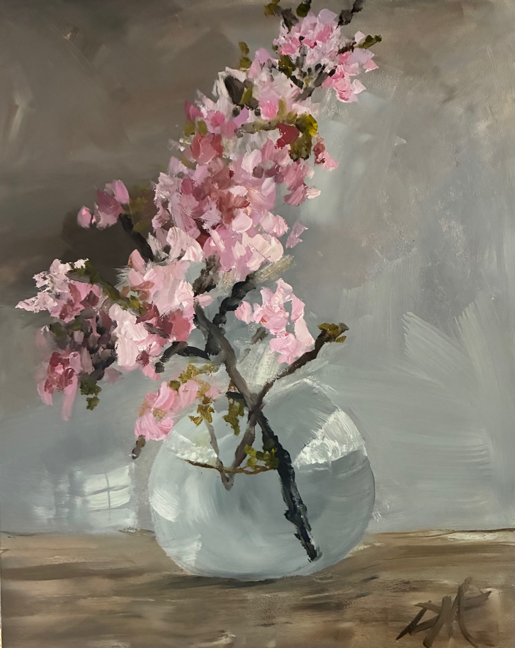 Pink cherry blossoms in a round glass vase on a wooden surface, with a gray background.