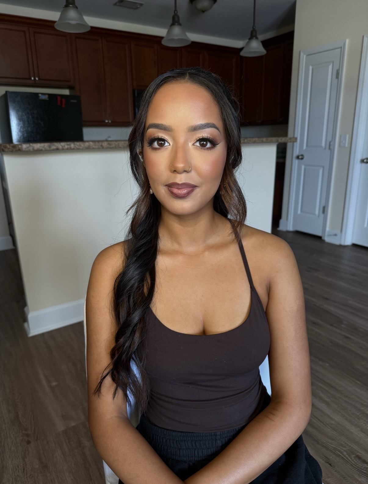 Young woman with long dark hair in a braid, wearing a black tank top, standing in a home interior.