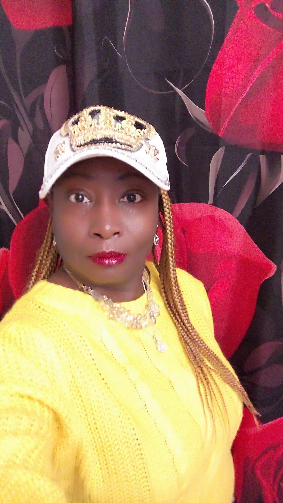 Woman in yellow dress with headscarf and jewelry, lying on black and red fabric, looking at camera.