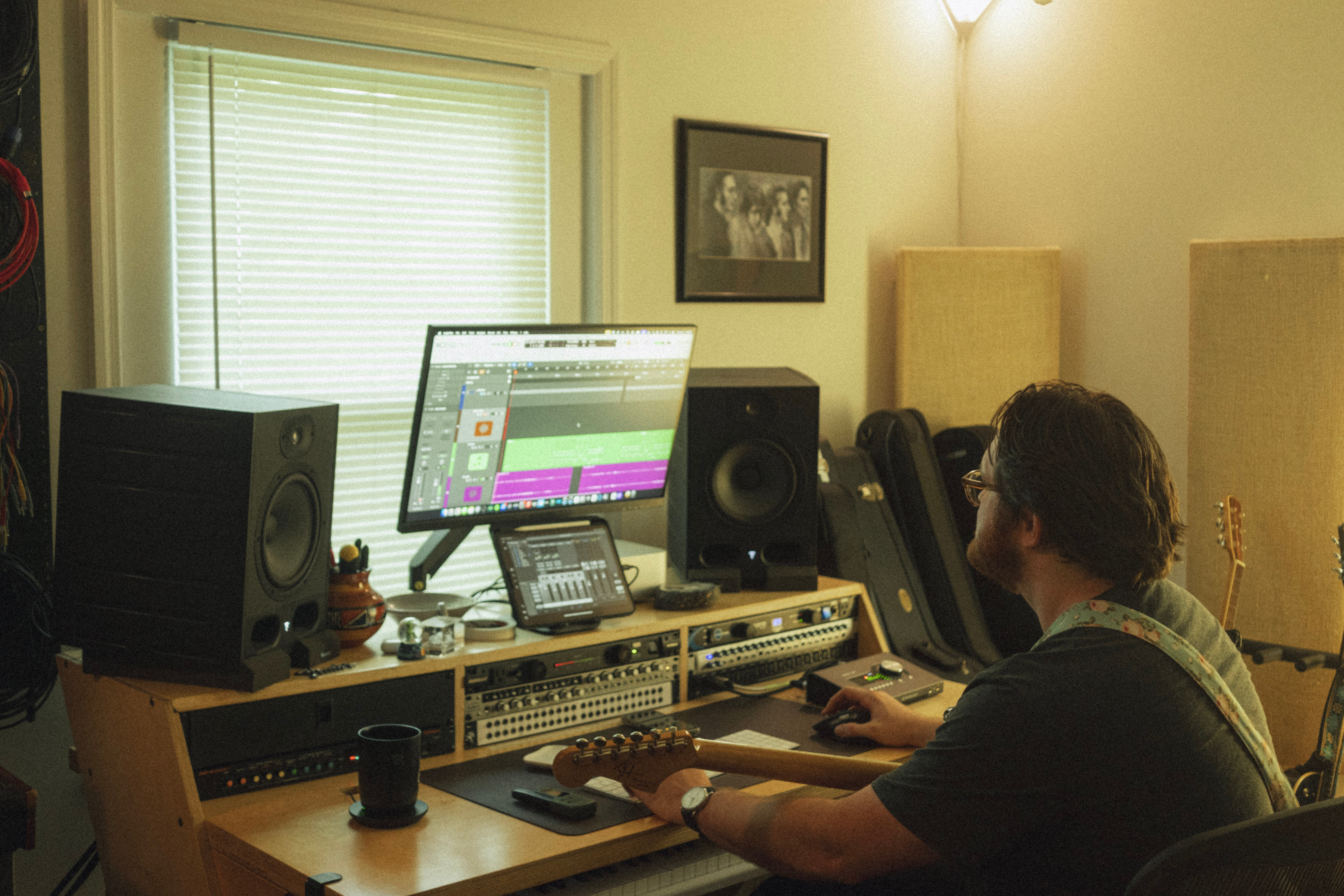 Person working at a music studio with computer, speakers, and audio equipment, sitting at a desk with a window behind. Word count: 20