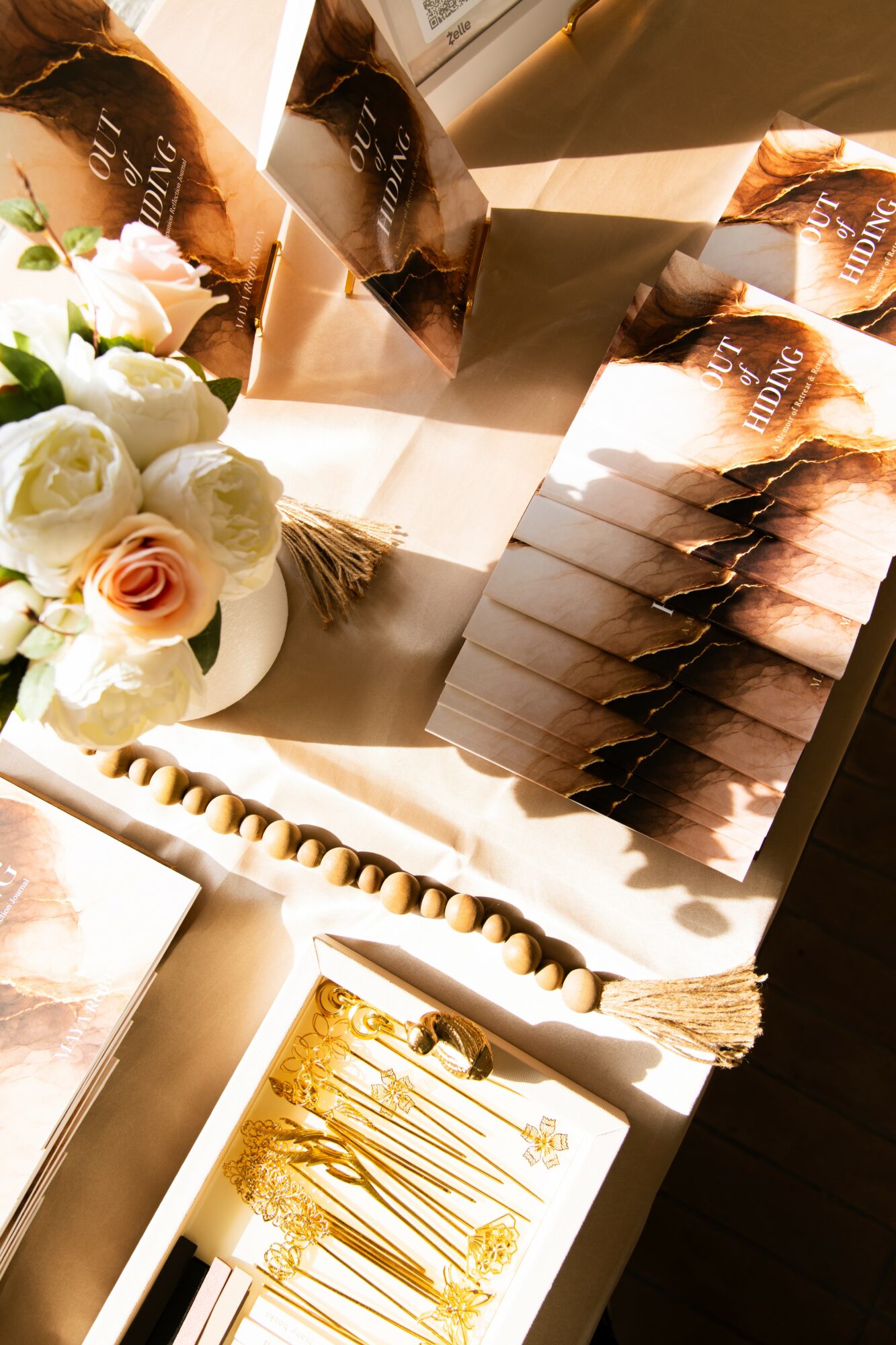 Display of chocolate cakes, a bouquet of white roses, and a decorated cake with gold accents on a table.