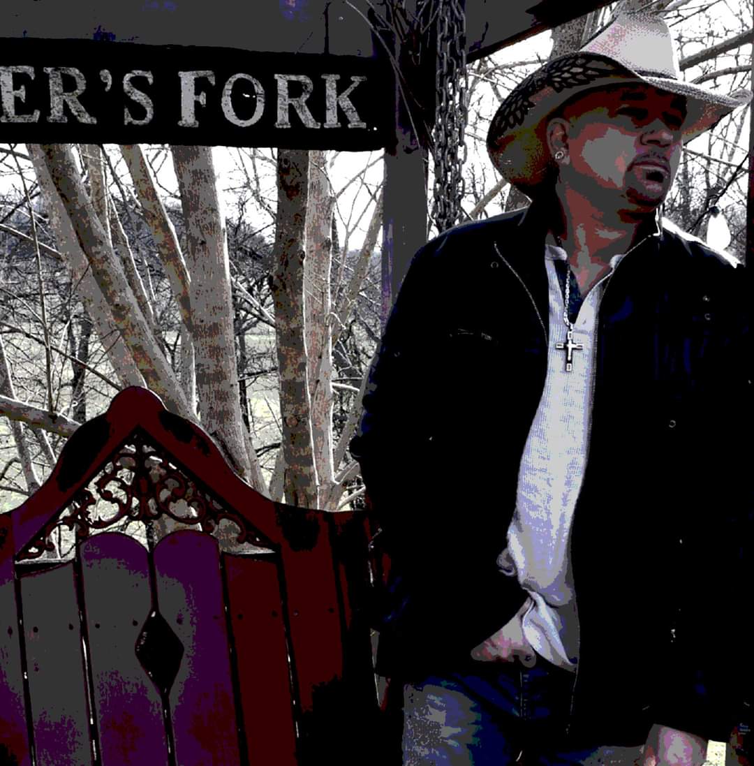Man wearing a hat and jacket standing outdoors near trees and a sign that reads 'FORK'.