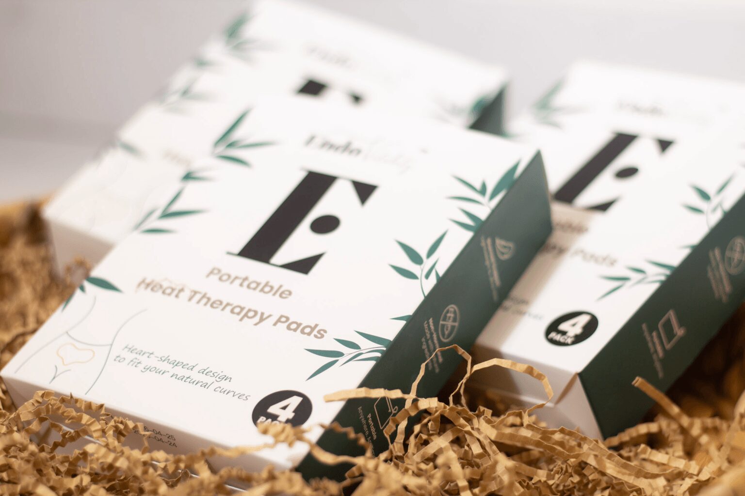 Boxes of portable heat therapy pads with green leaf designs on a bed of shredded paper.