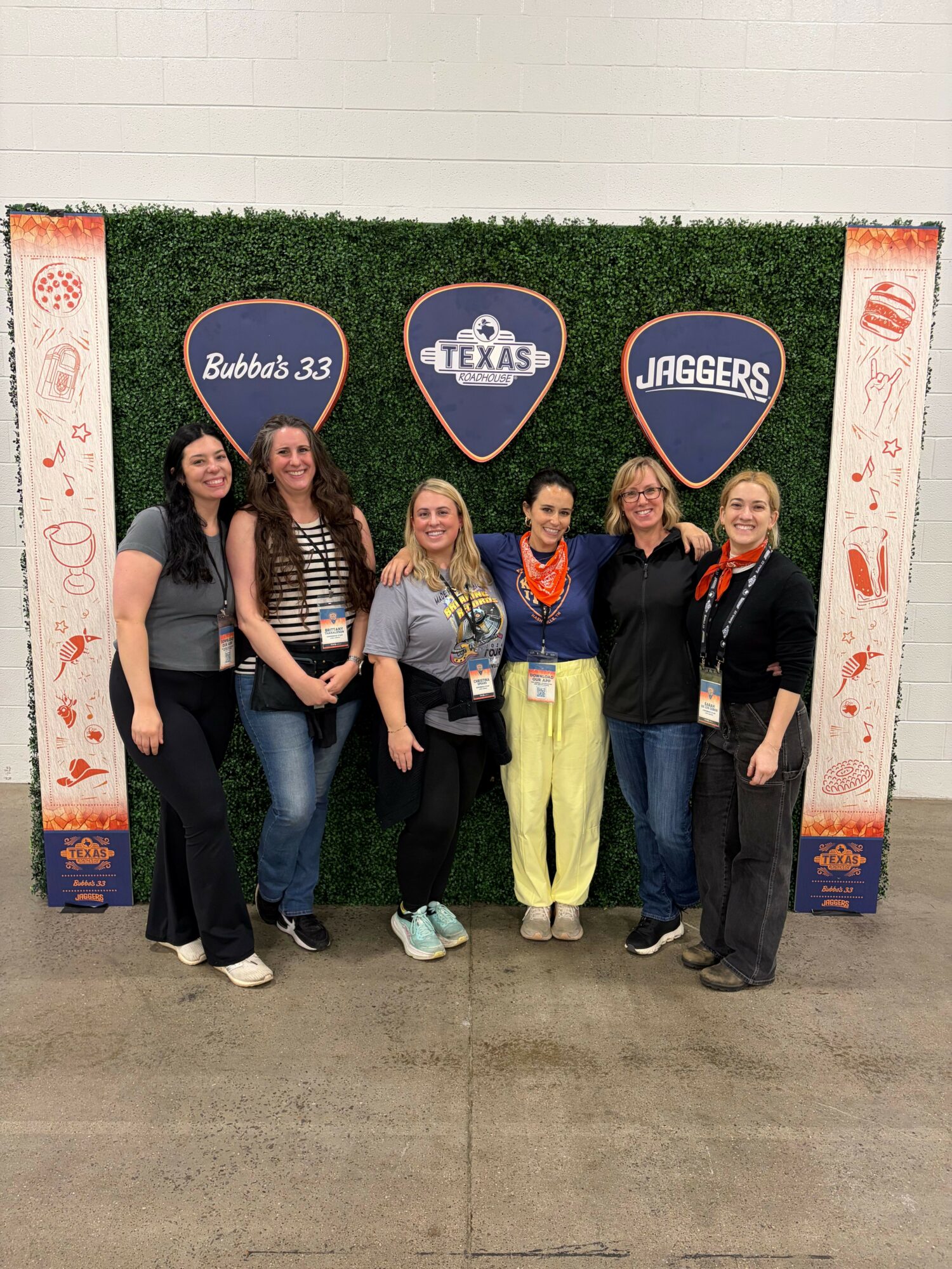 Group of five women standing in front of a backdrop with logos and text, smiling and posing for a photo.