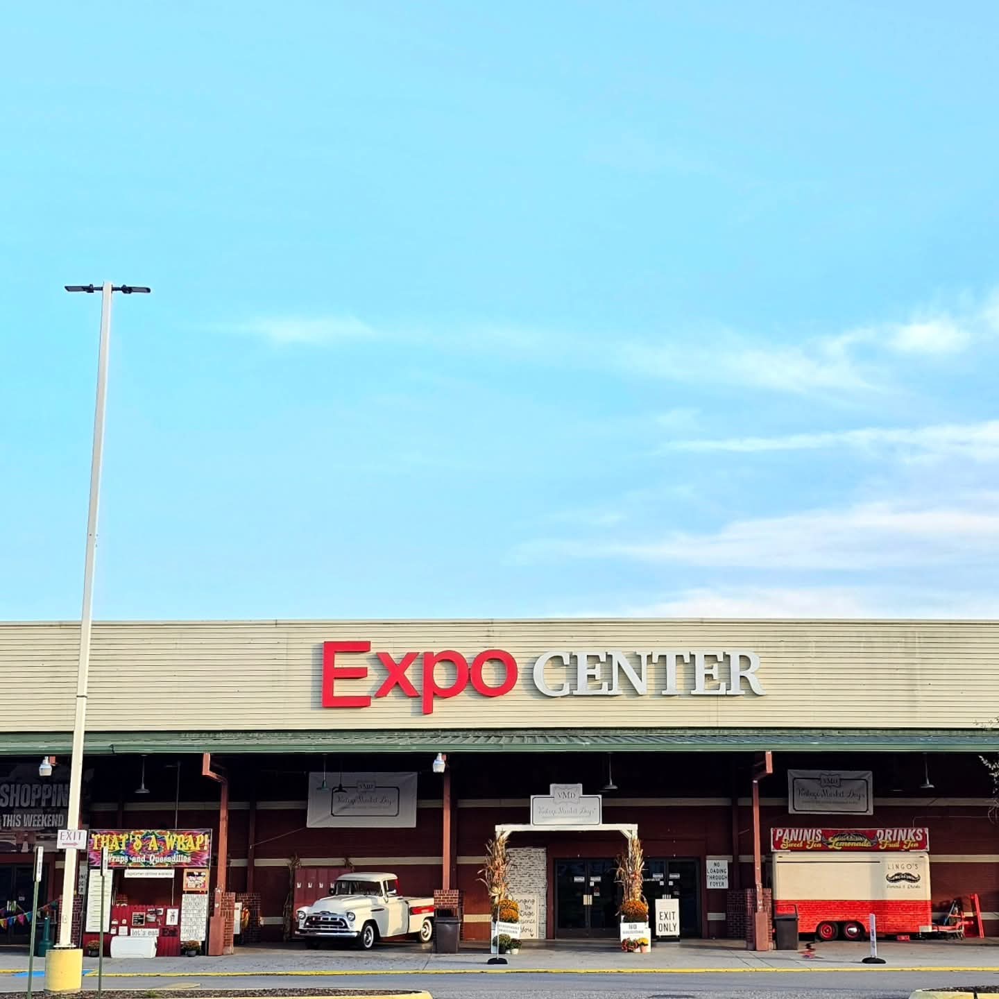 Exterior view of Expo Center building with a clear blue sky, signage, and parked vehicles in front.
