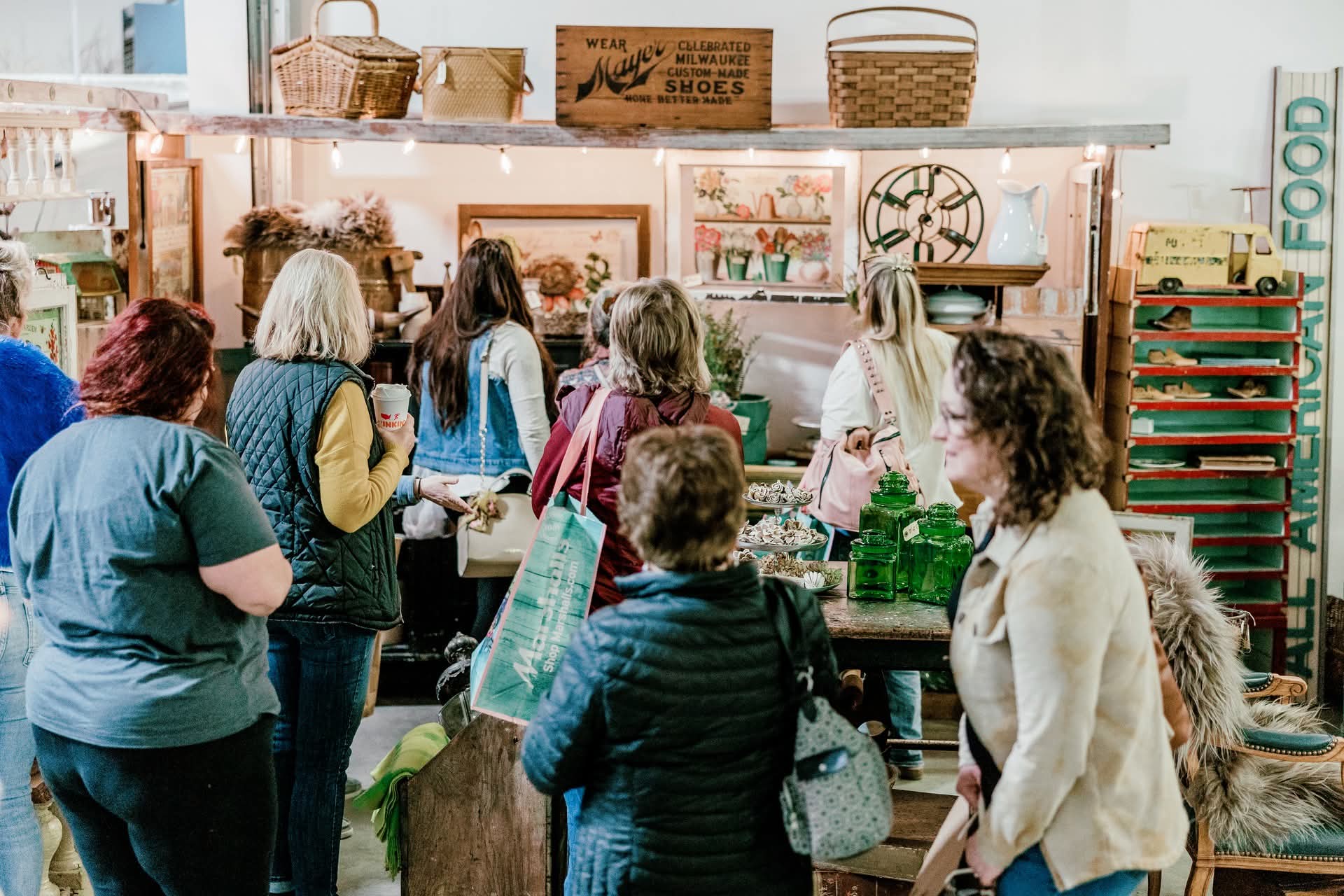 Group of people shopping at a store with shelves and artwork, some carrying shopping bags, in a well-lit space.