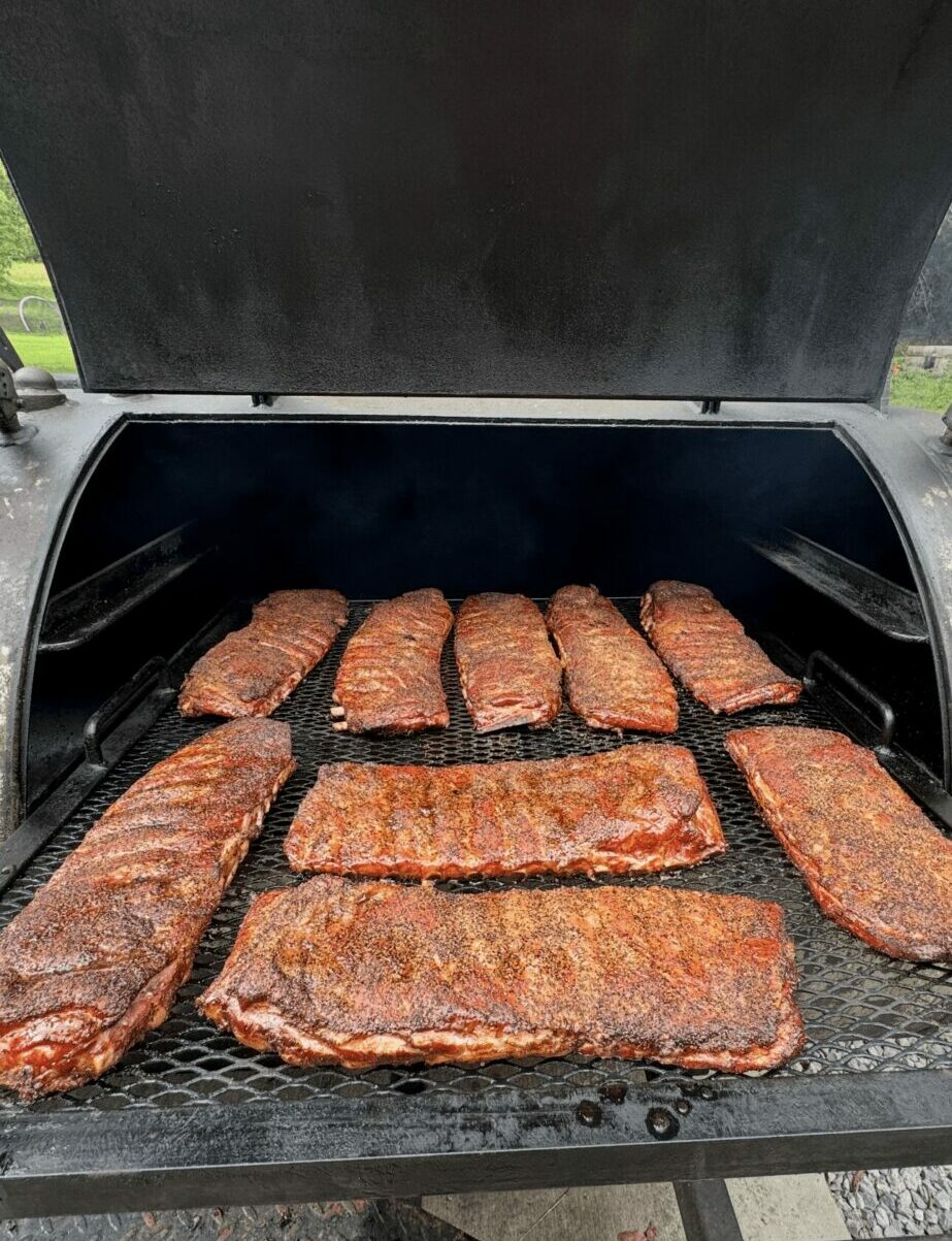 Barbecue grill with several cooked meat slices inside, some with grill marks, on a black surface.