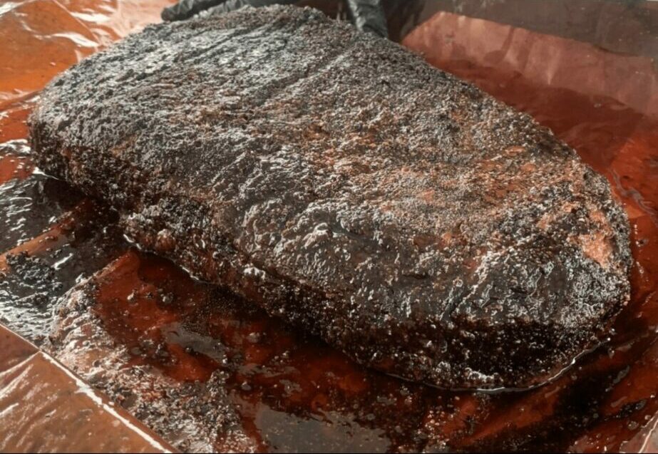 Cooked, seasoned meat resting on a wooden surface with juices around it.