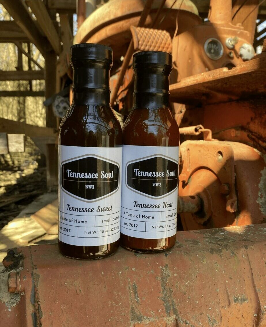 Two small bottles with white labels and black caps placed on a brick surface outdoors, with a large orange construction vehicle in the background.