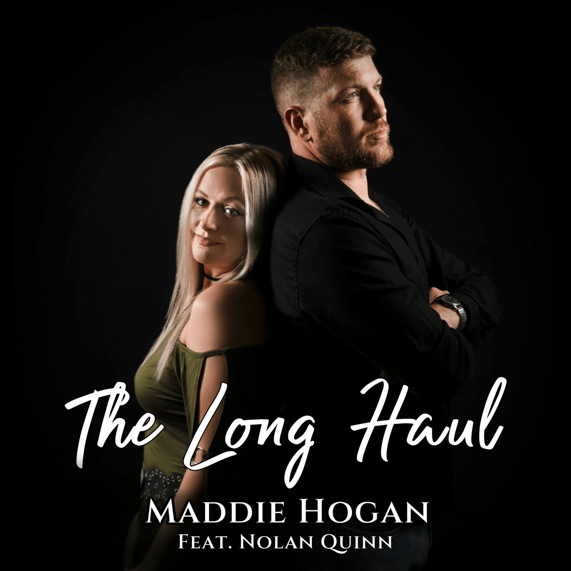 A man and woman stand back-to-back against a black background, with the woman smiling and the man looking away.