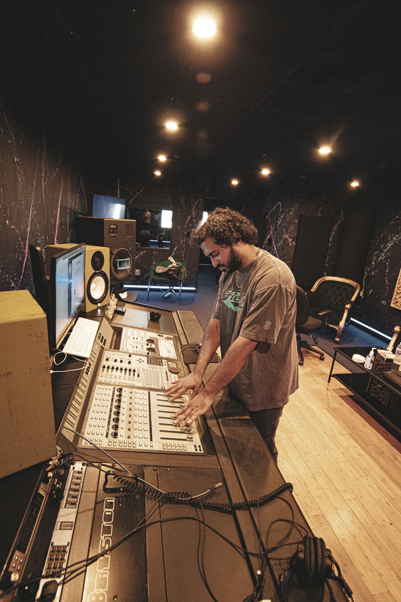 Person working at a mixing console in a recording studio with equipment and monitors, dimly lit room.