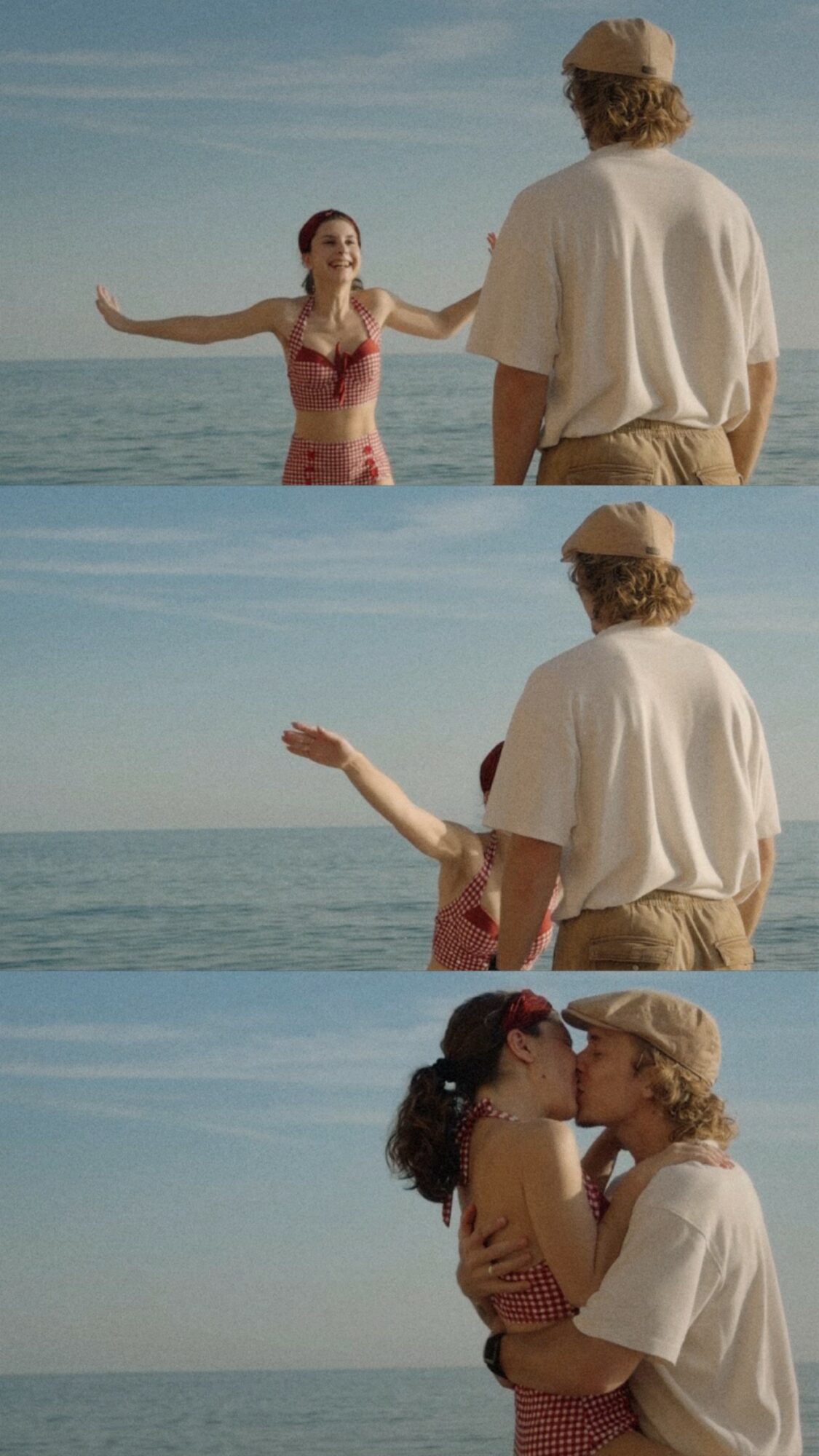 A woman in a pink dress stands in water with arms outstretched, facing a man in a white shirt and hat on the beach.