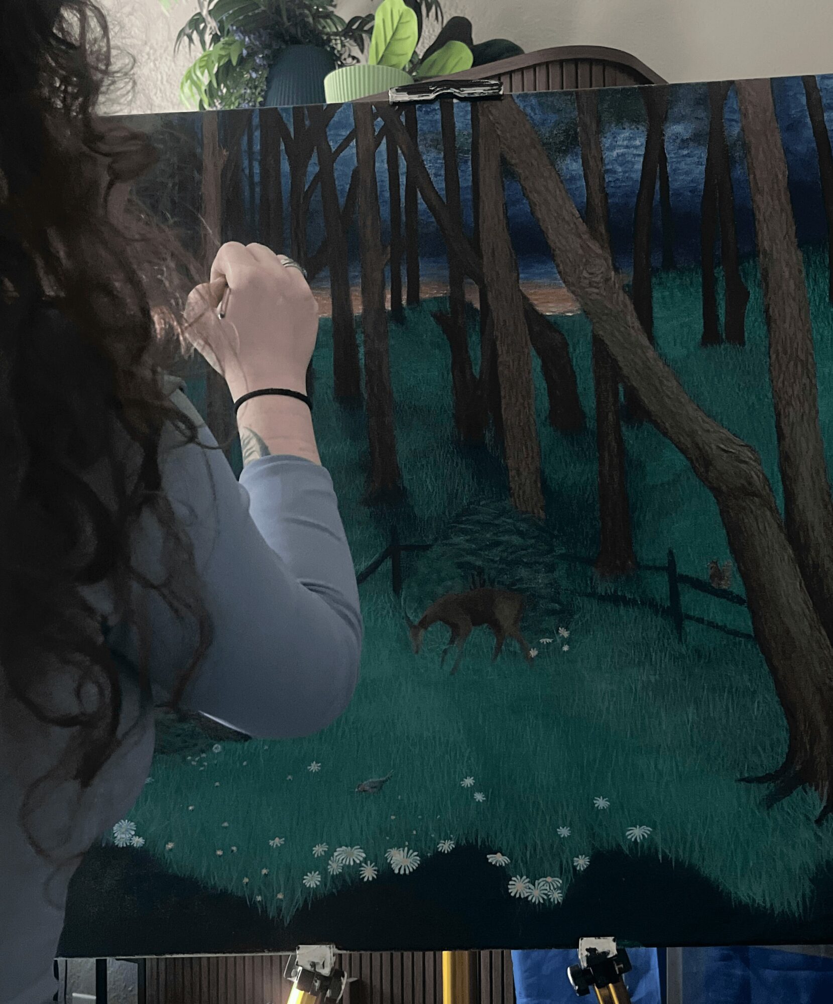 Person painting a forest scene with trees and a wolf in a dark, moody landscape, using a brush and canvas.
