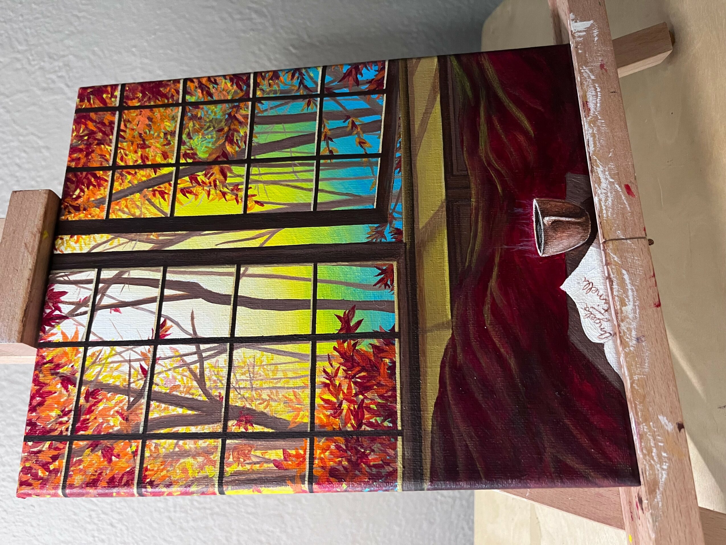 Colorful landscape painting of trees and sky, with a red and black abstract base, on a wooden easel.