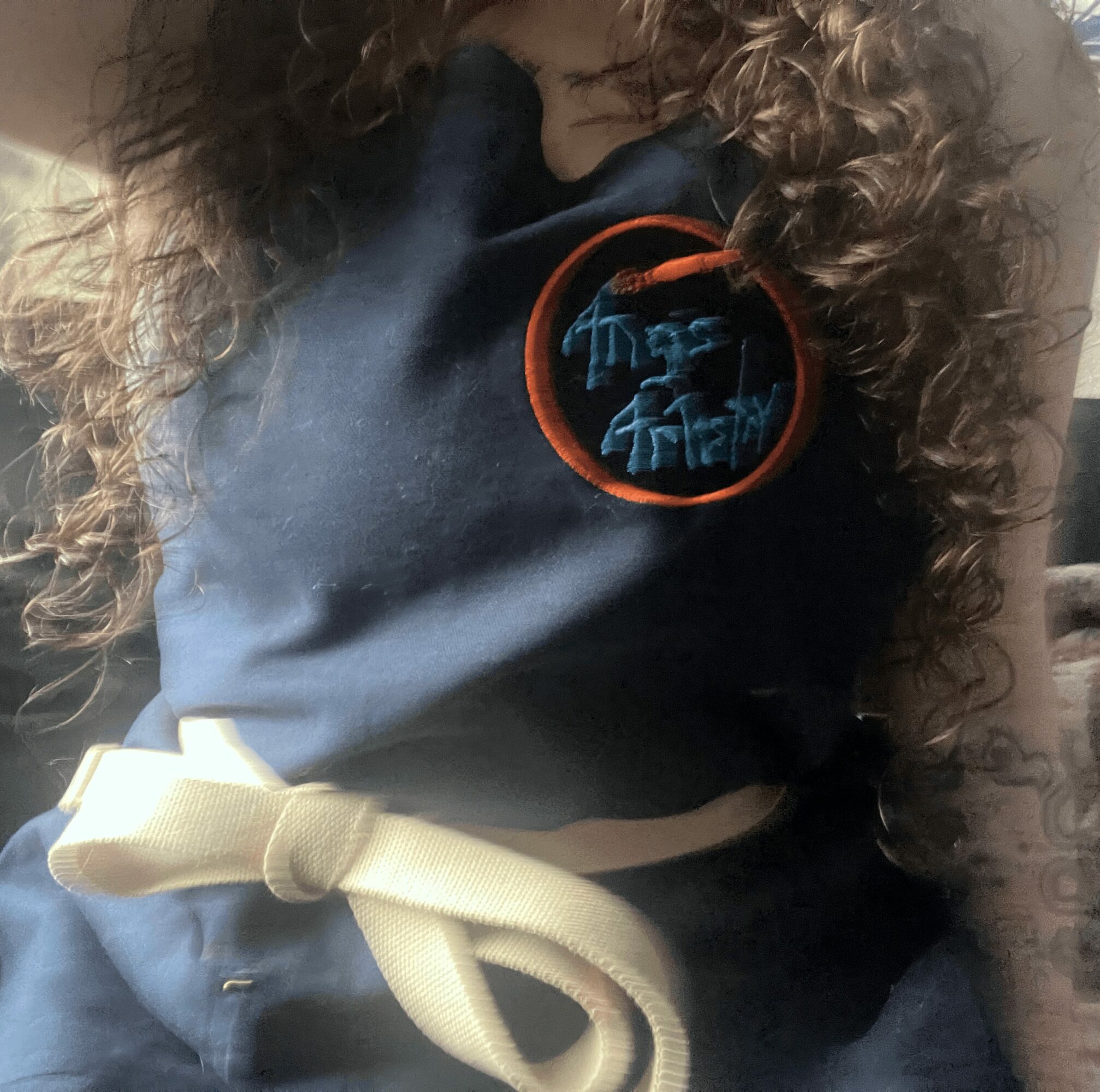Close-up of a person wearing a dark hoodie with a circular logo, curly hair, and a beige drawstring, indoors.