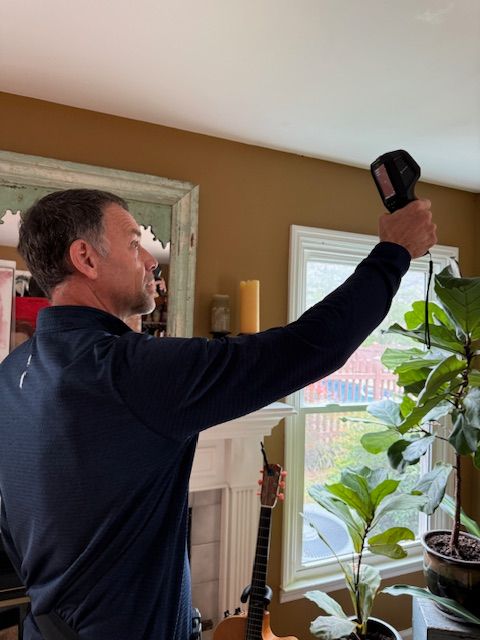 Person holding a black object near a window with plants and a candle, seen from the side.