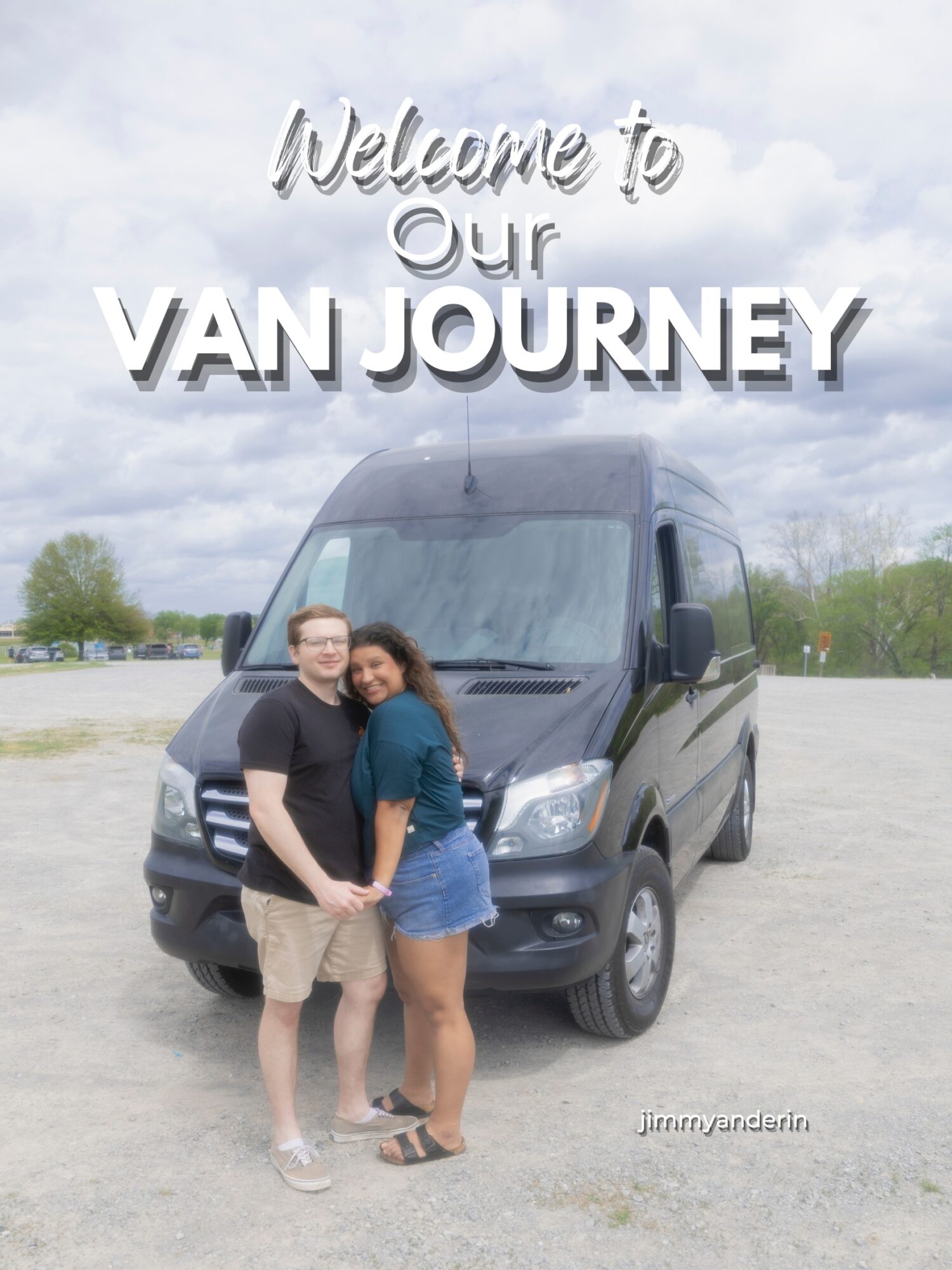 Two people stand in front of a black van outdoors, smiling, with a cloudy sky and trees in the background.