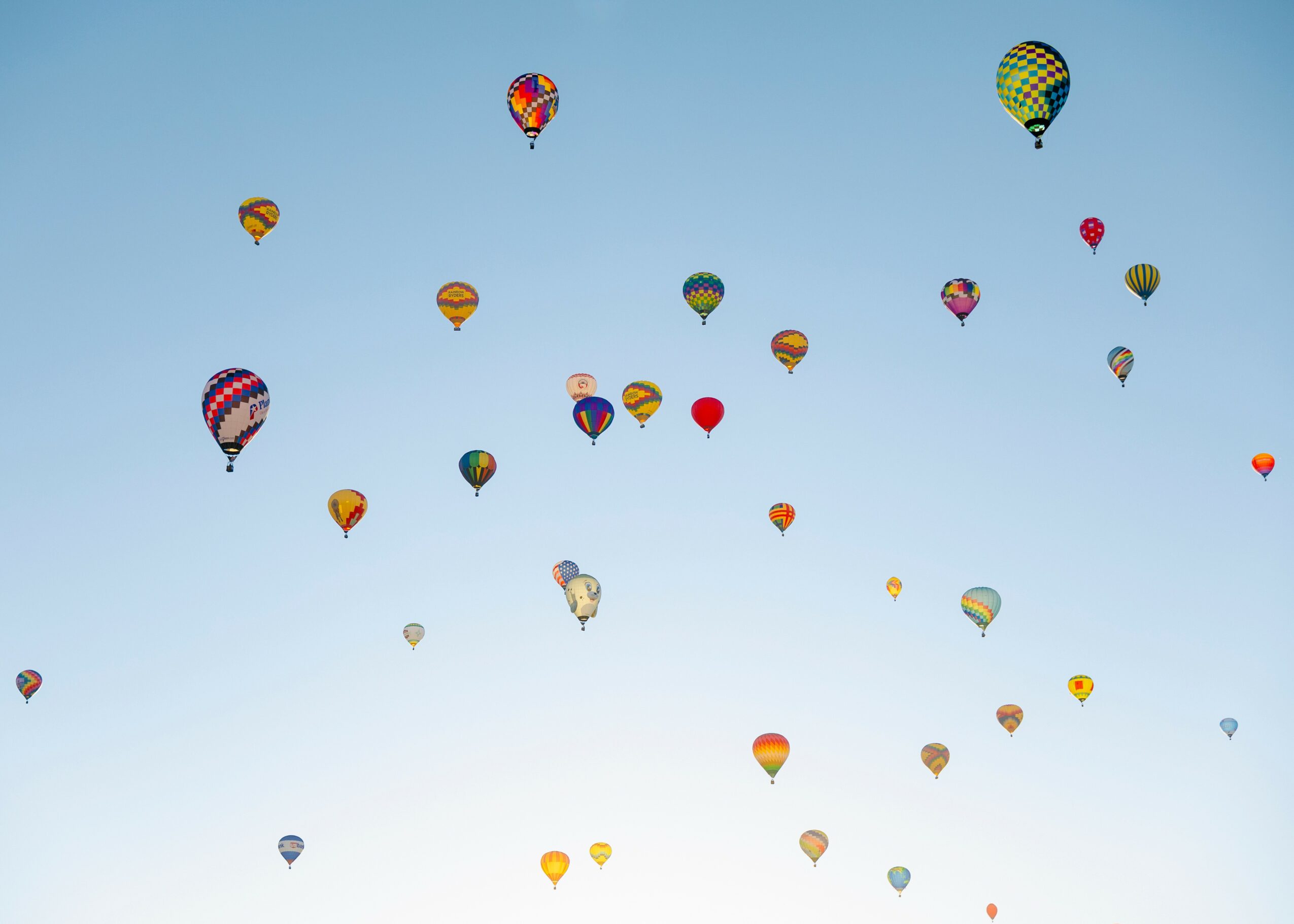 Numerous colorful hot air balloons floating in a clear blue sky.