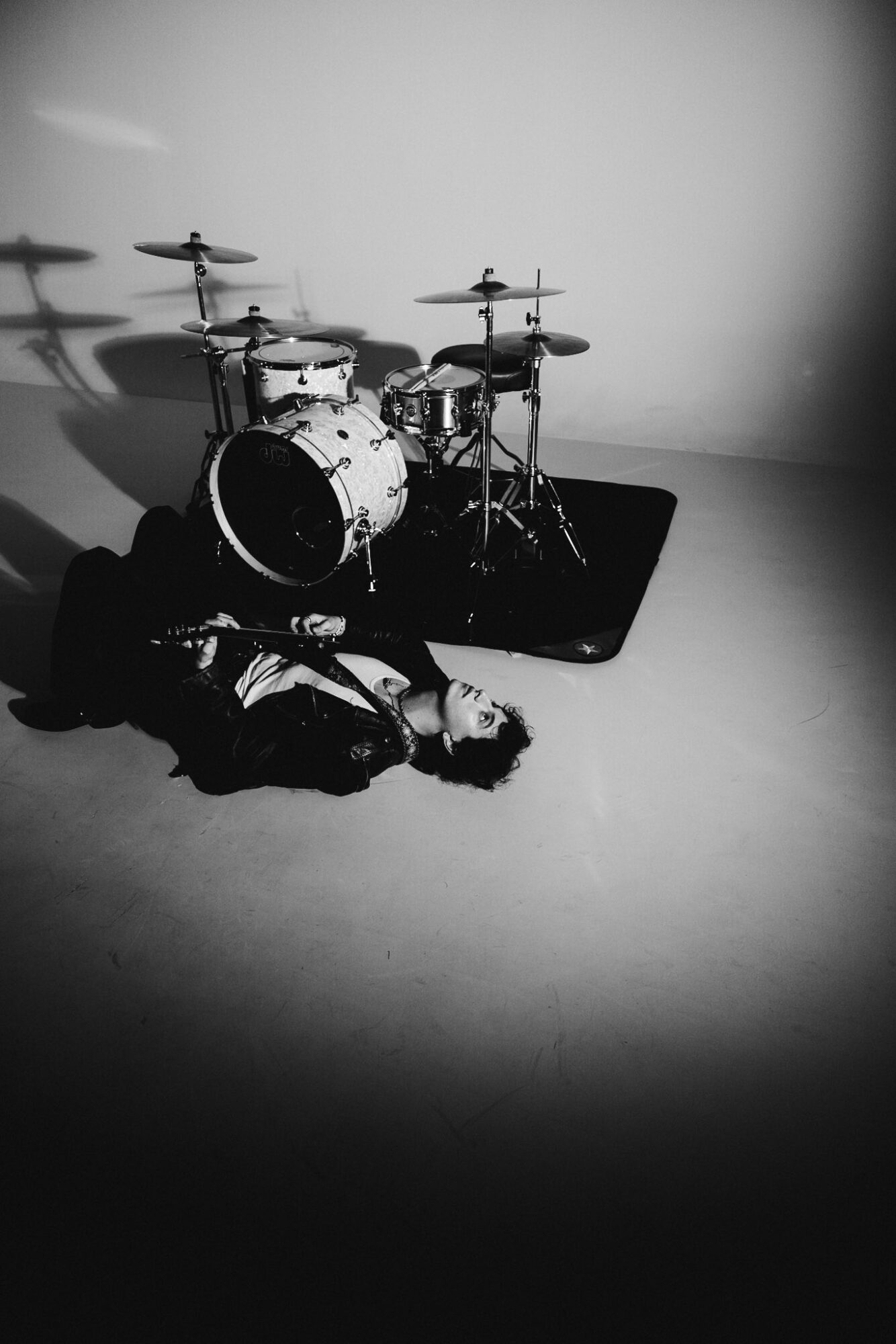 Person lying on the floor with a drum set in the background, in a black and white photo.