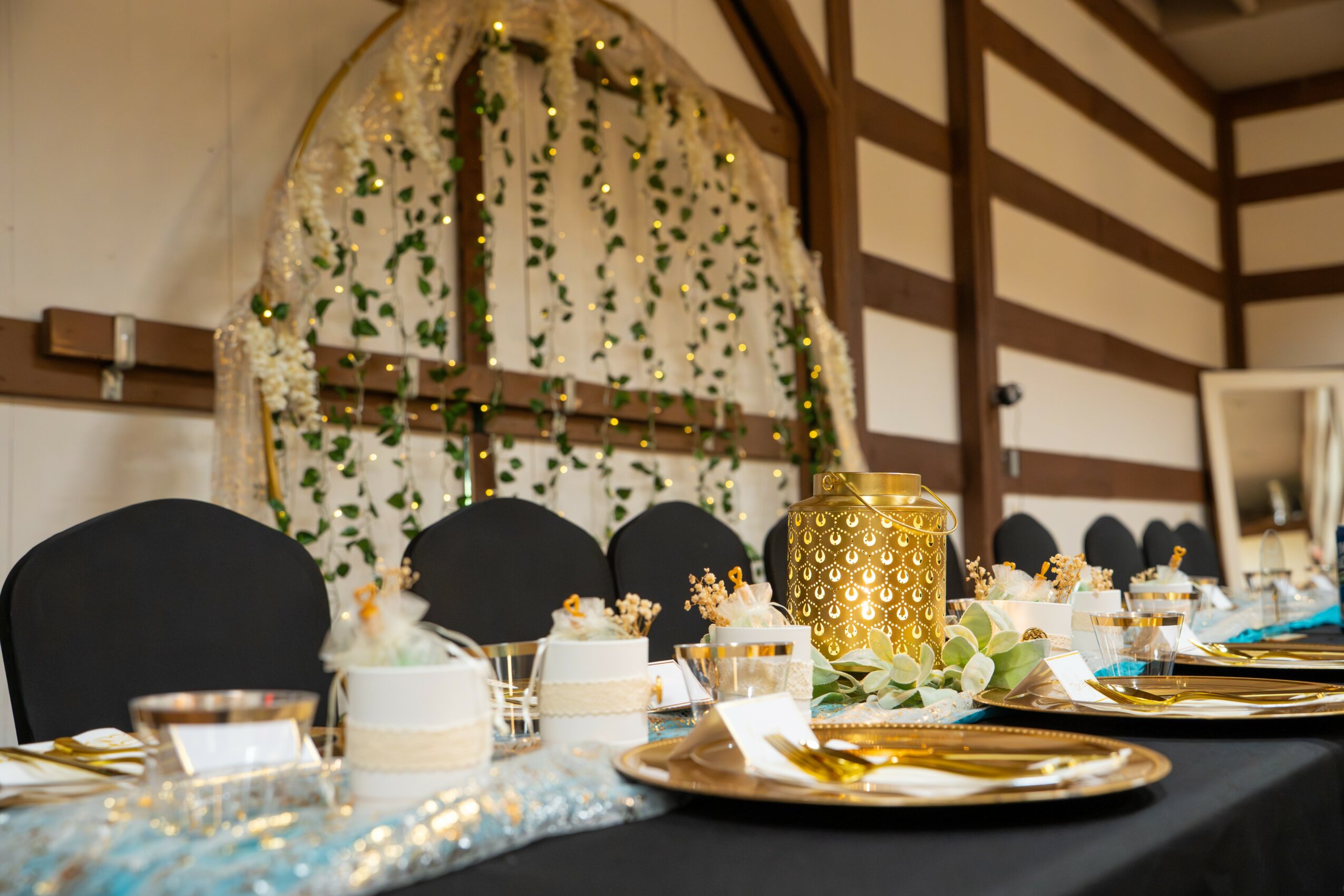 Table with gold and white decorations, black chairs, and a floral backdrop, set for an event or celebration.