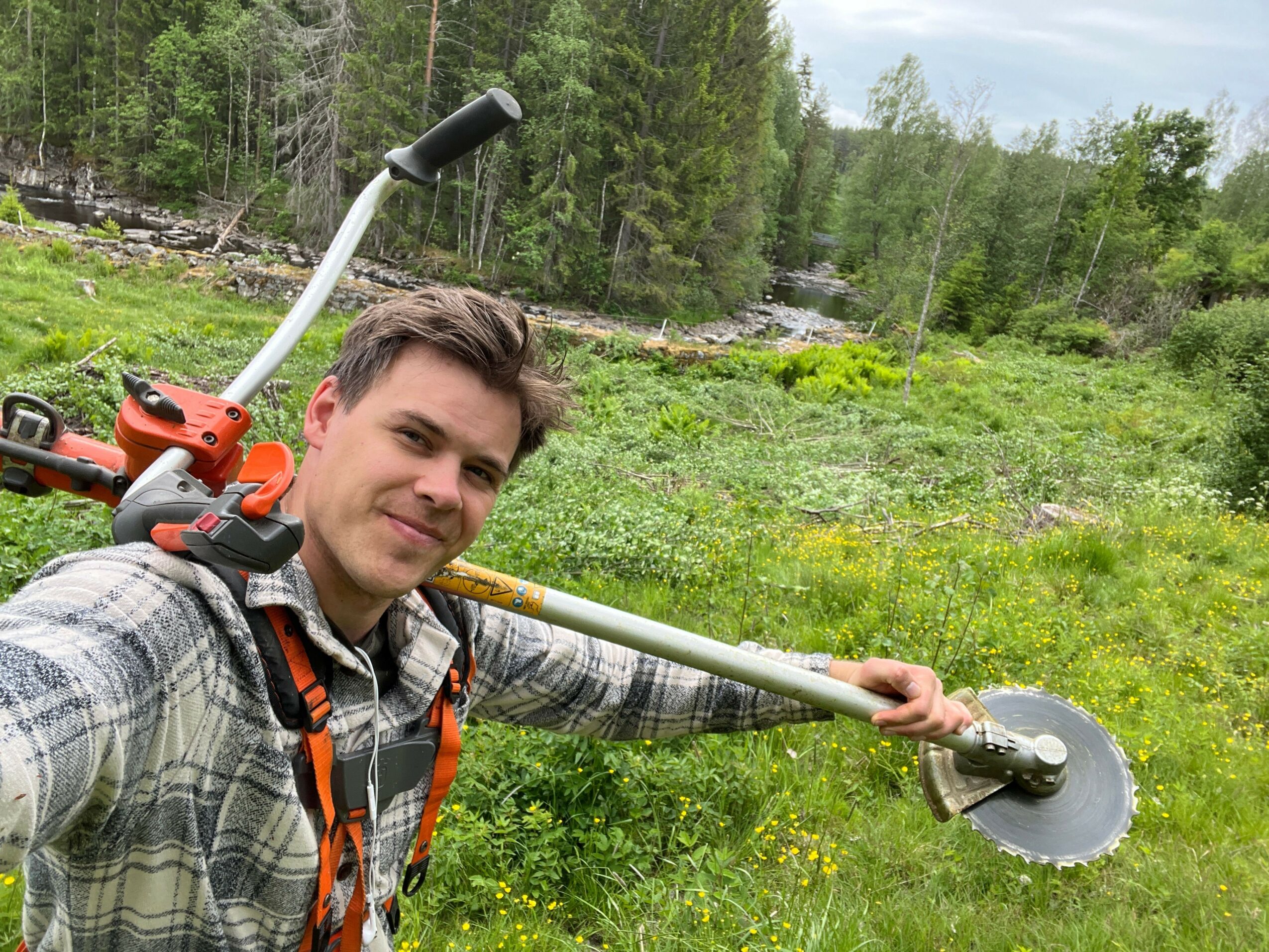 Person outdoors holding a gardening tool with a green grassy background.