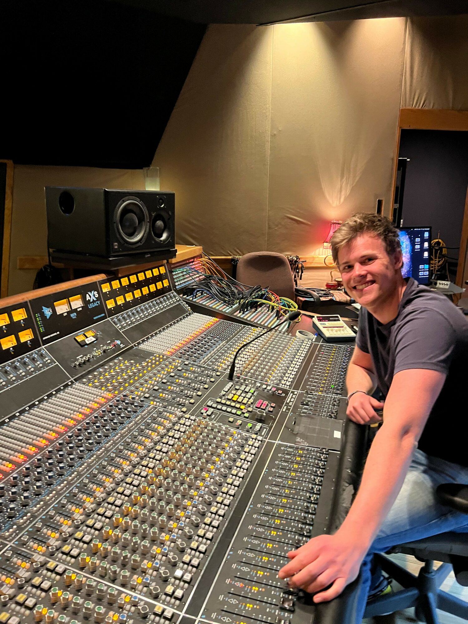 Person operating a large audio mixing console in a recording studio, with equipment and a speaker visible in the background.