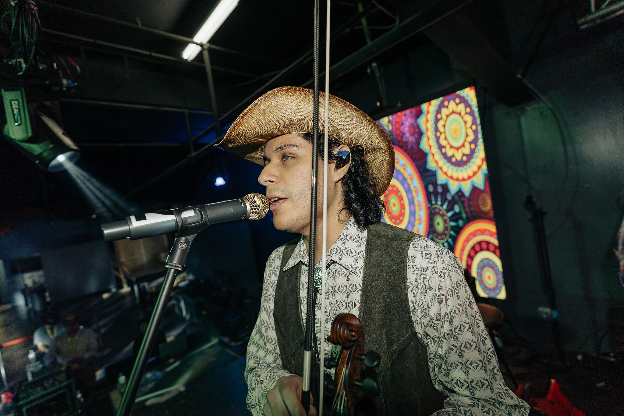 Musician wearing a cowboy hat singing into a microphone on stage with colorful background display