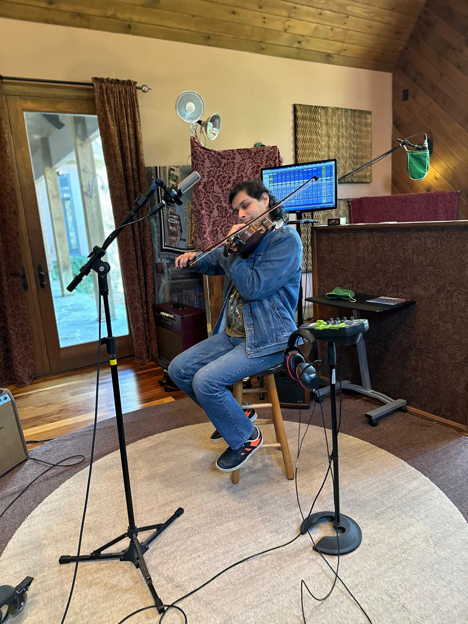 Person playing flute in a cozy room with wooden ceiling, computer monitor, and microphone setup.