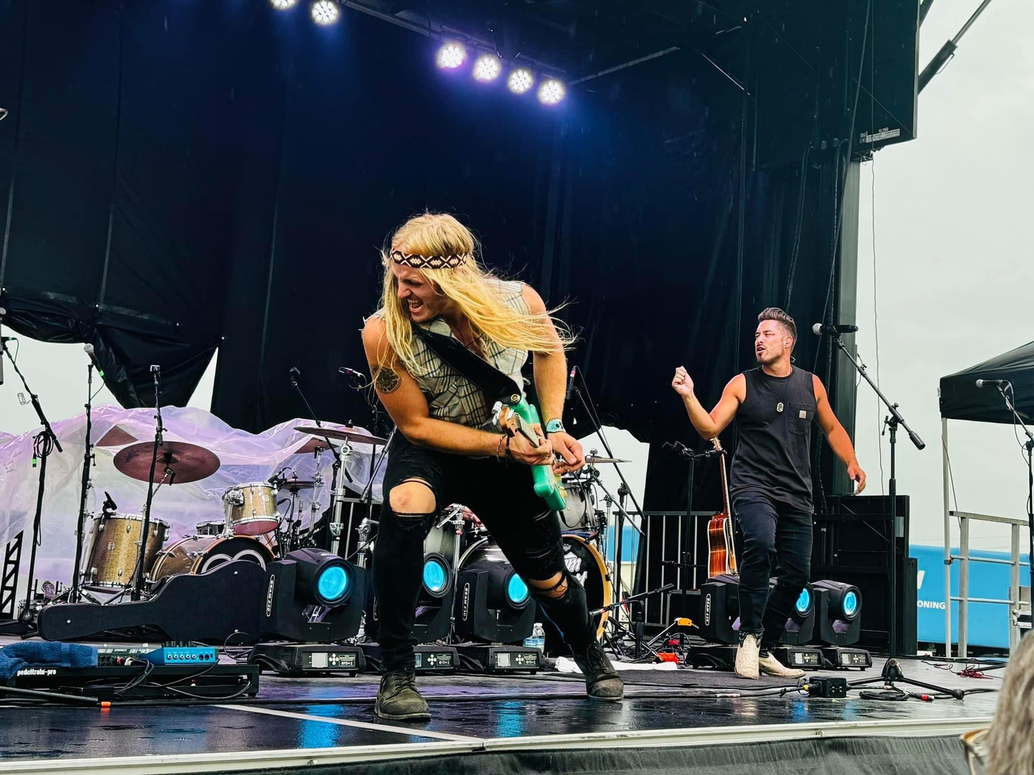 Two performers on stage, one singing into a microphone and the other dancing, with musical instruments in the background.