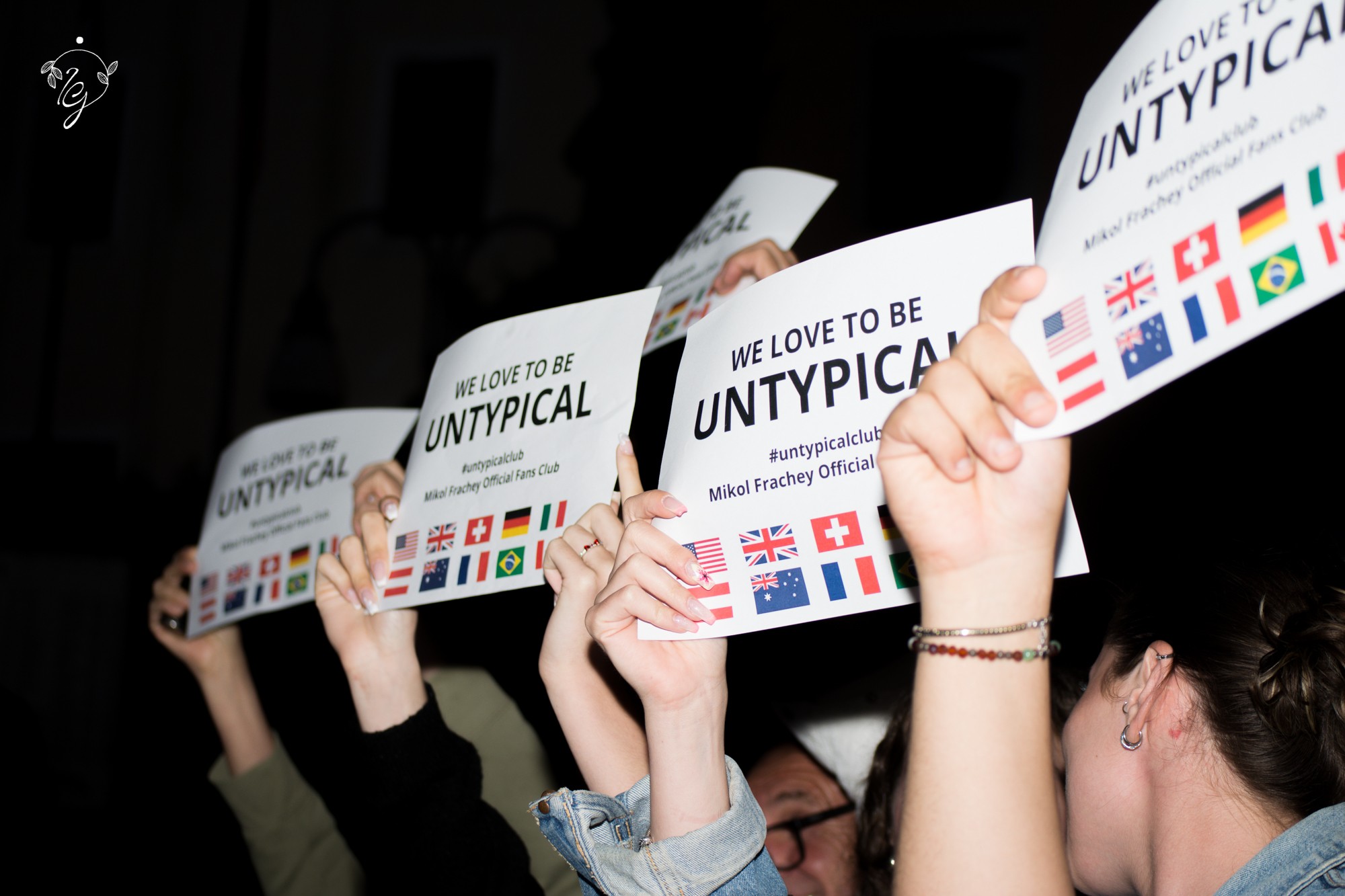 People holding signs with flags and text, raising them in a group, in a dark setting.