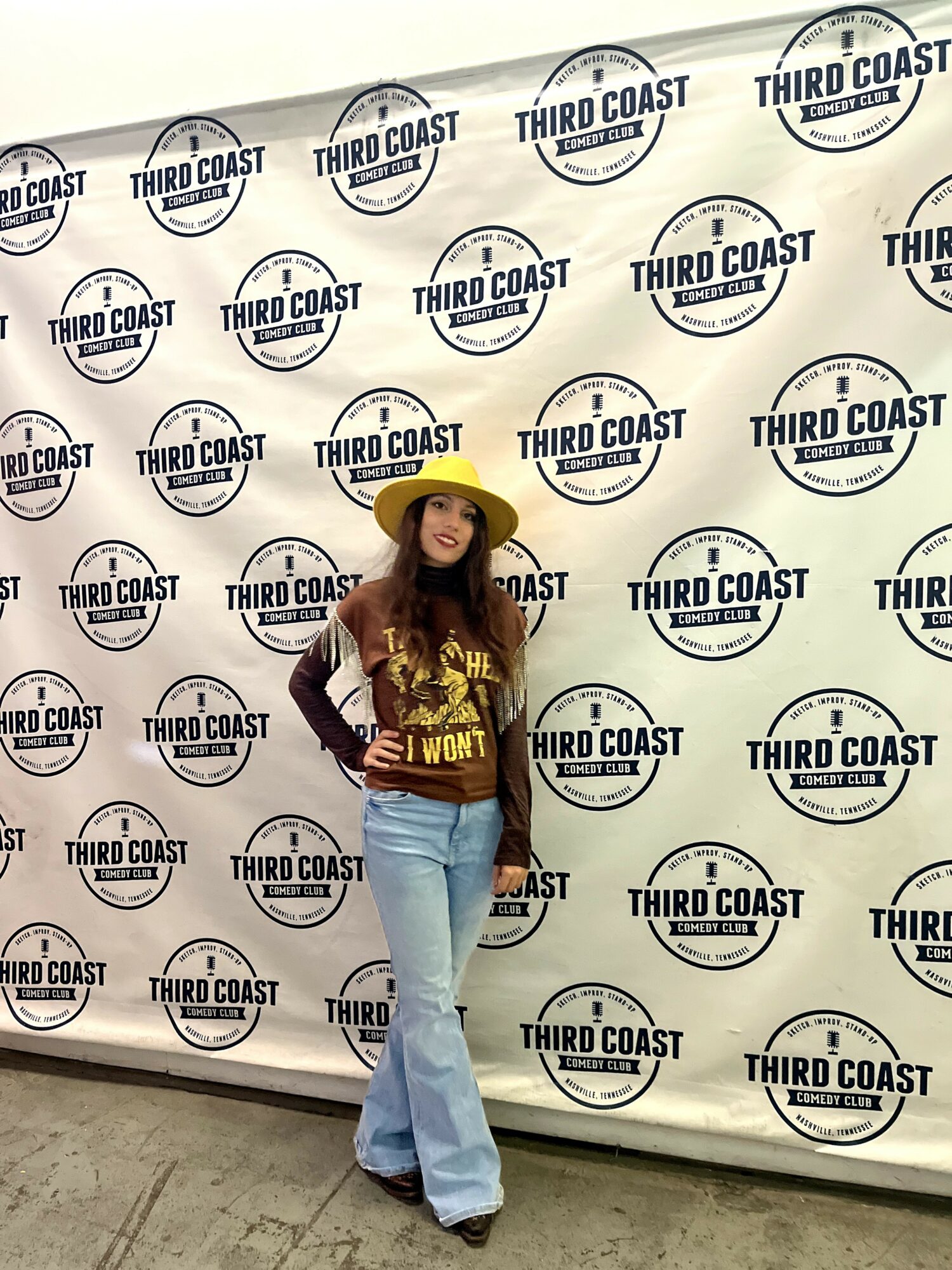 Woman wearing a yellow hat and maroon top standing in front of a backdrop with 'Third Coast' logos.