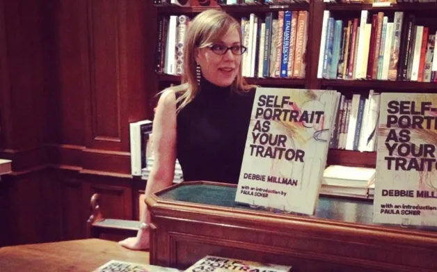 Woman with glasses standing behind a book display in a library, bookshelves in background.