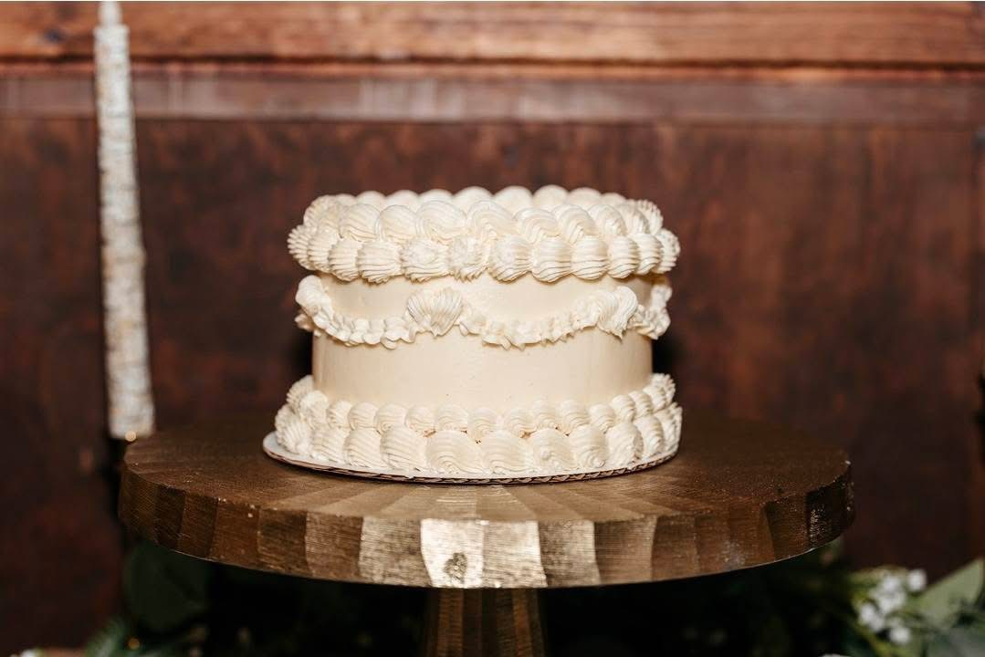 Two-tiered cake with white frosting and decorative piping on a wooden table, against a wooden background.