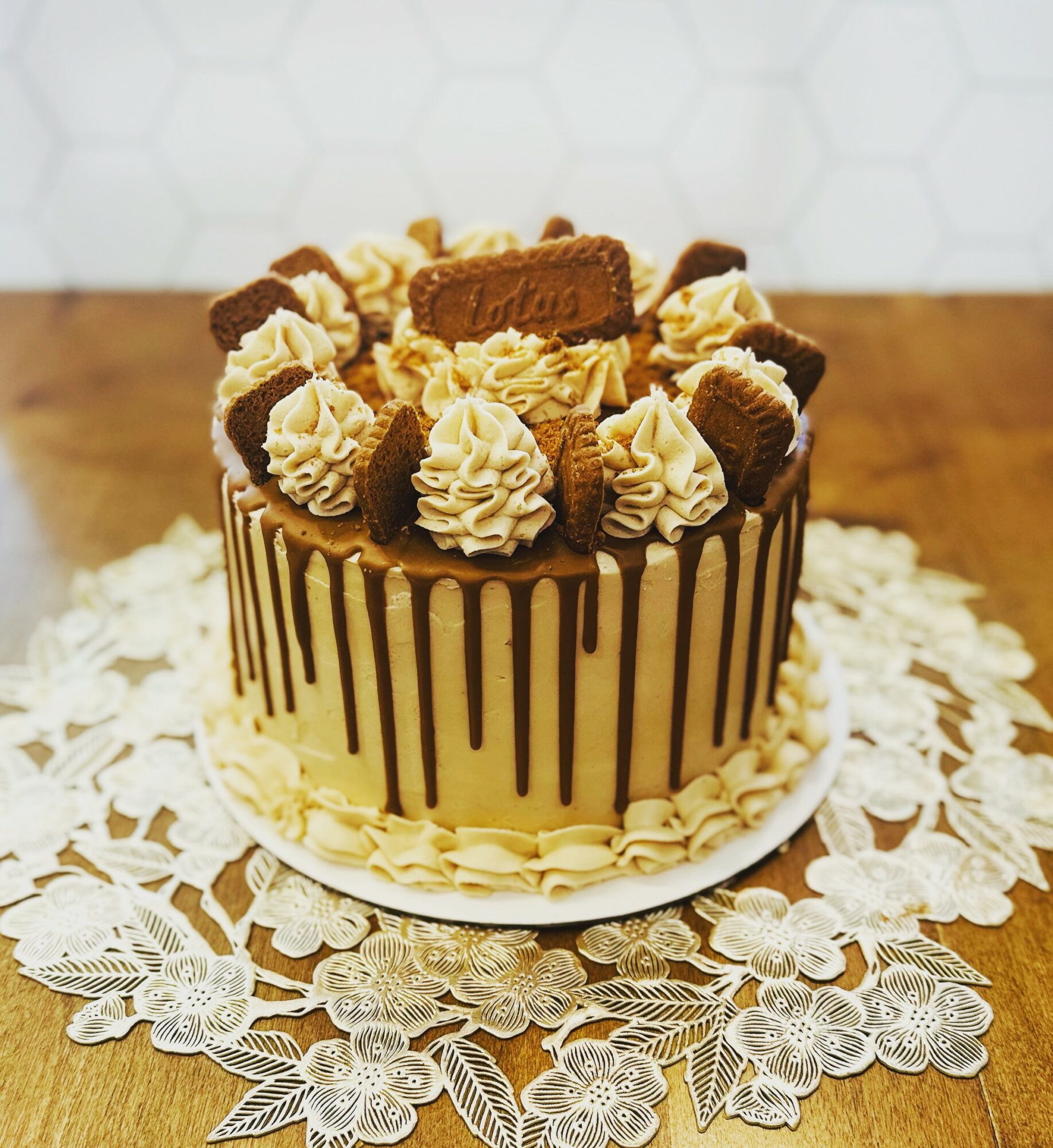 Cake with chocolate drizzle, cream decorations, and biscuit toppings on a lace doily, on a wooden surface.